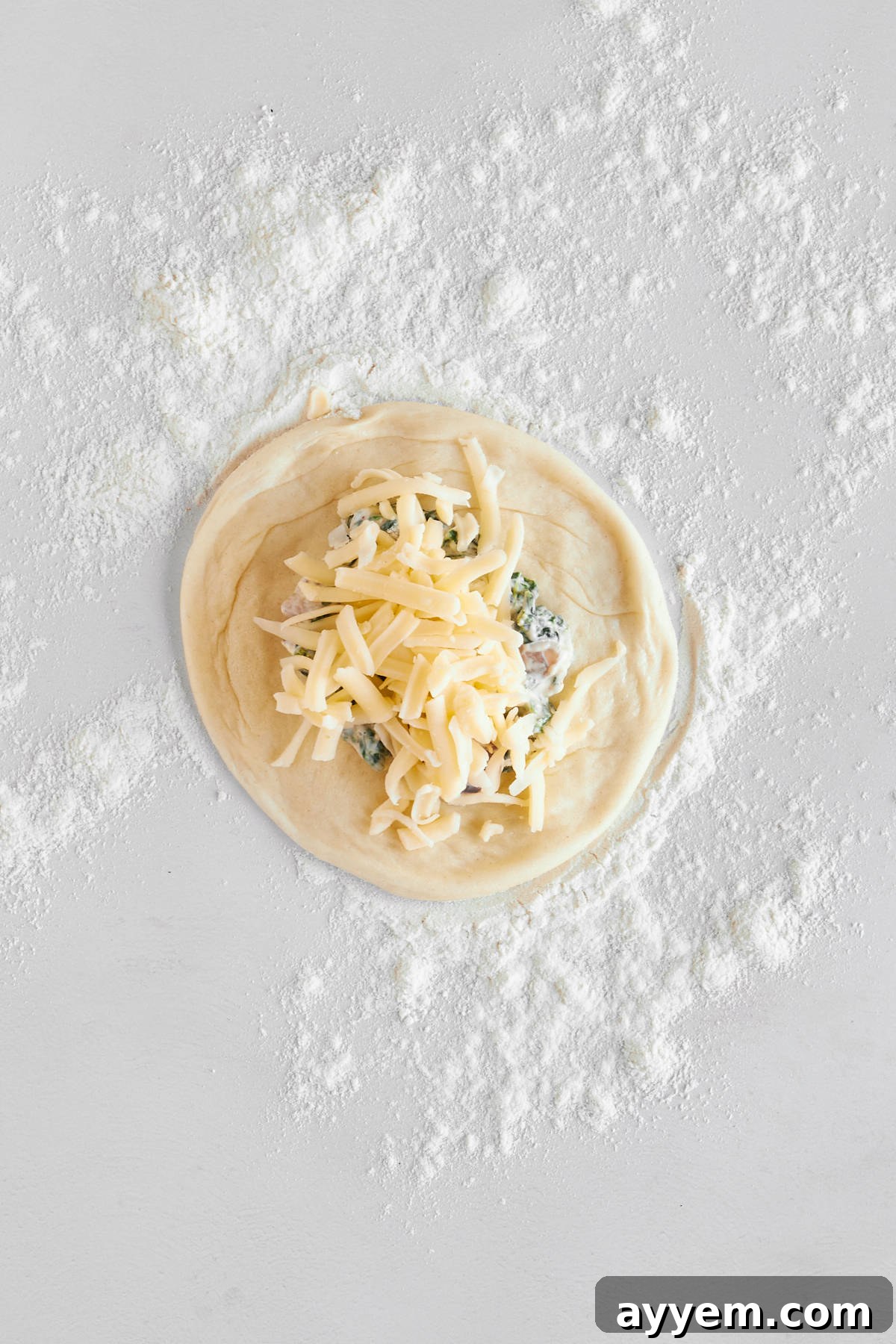 A flattened dinner roll on a floured surface, generously topped with a savory spinach and cheese mixture and shredded mozzarella.