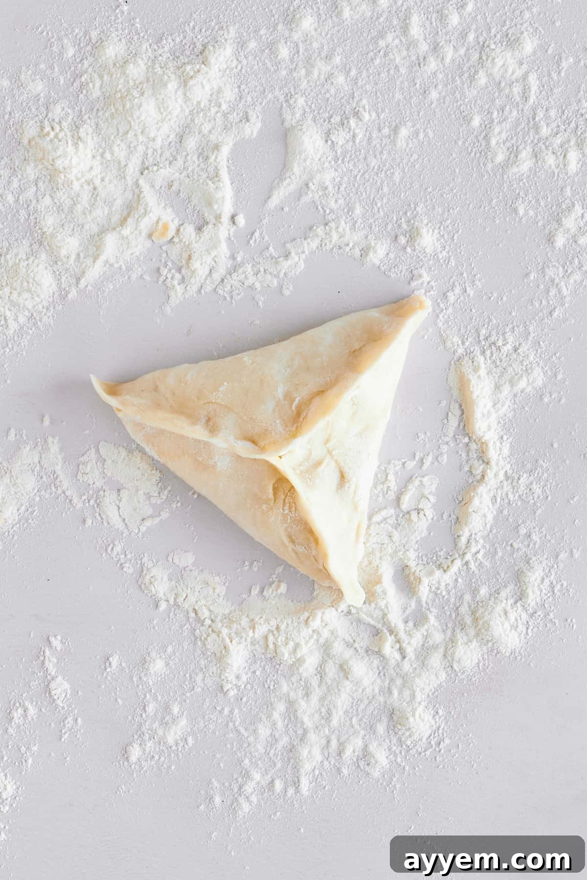 A raw fatayer pastry, expertly folded into a triangular shape with neatly crimped edges, ready for baking.