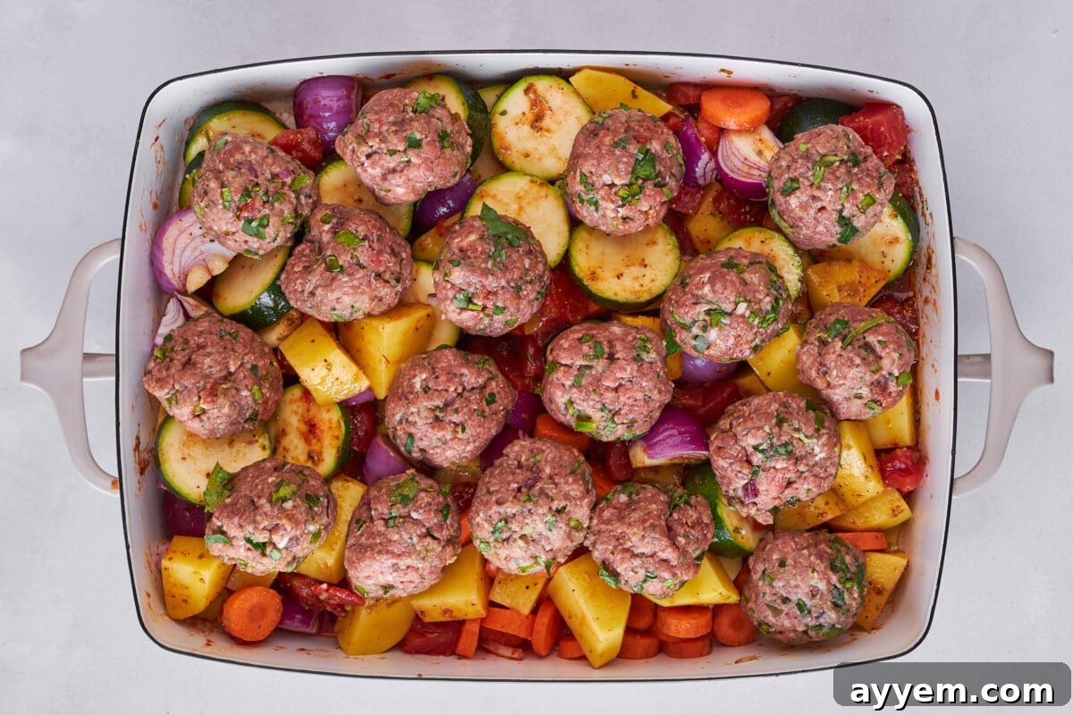 Raw kofta meatballs placed over vegetables in a baking dish.