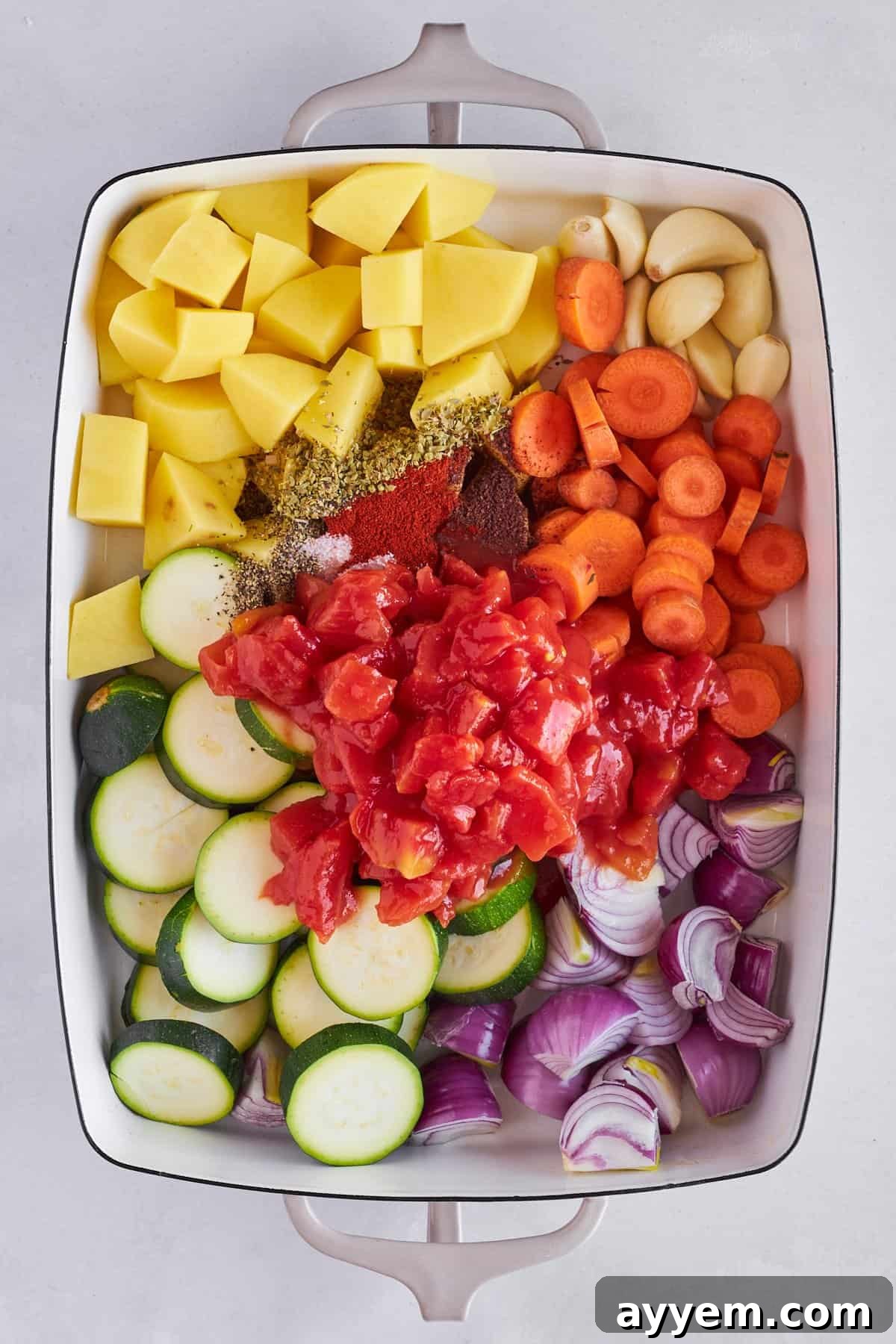 A vibrant mix of seasoned vegetables including zucchini, potatoes, carrots, onions, and tomatoes in a baking dish, ready for the oven.