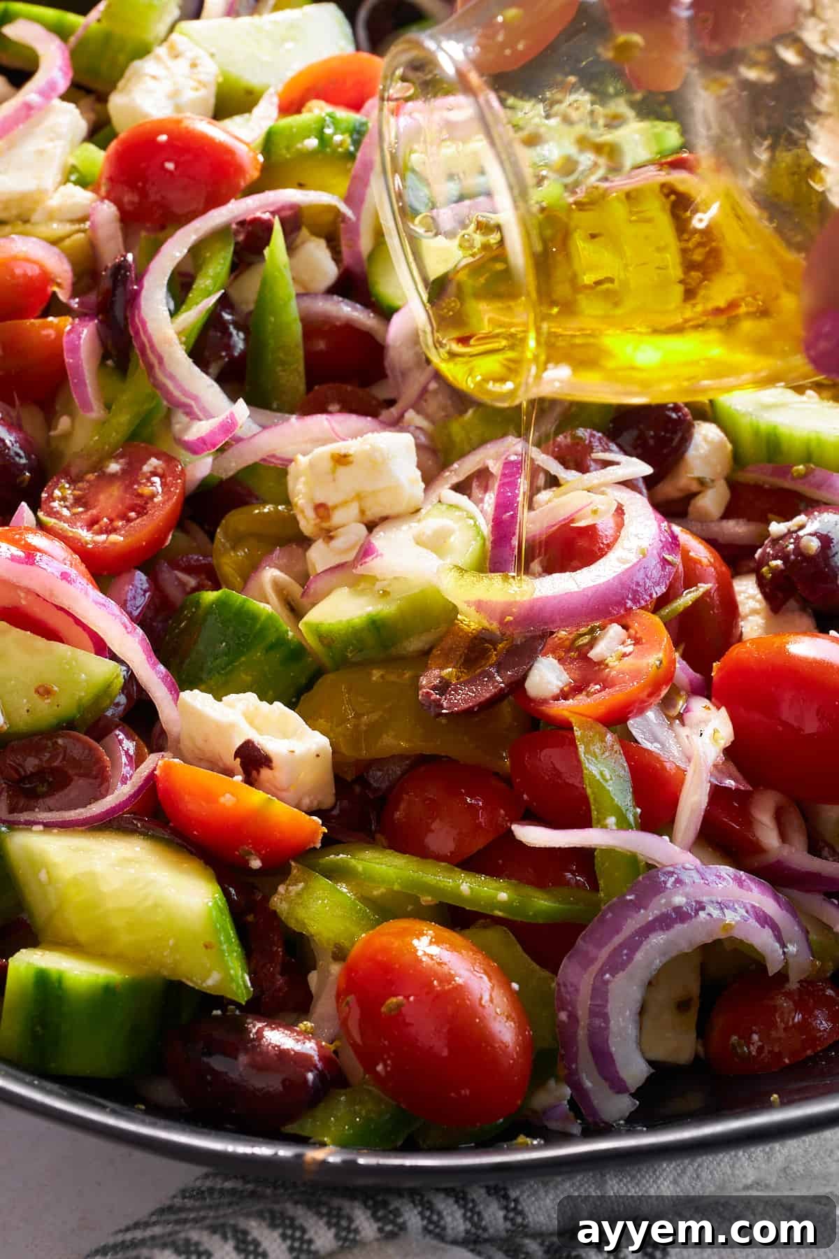 Vinaigrette being poured over a Greek salad. 