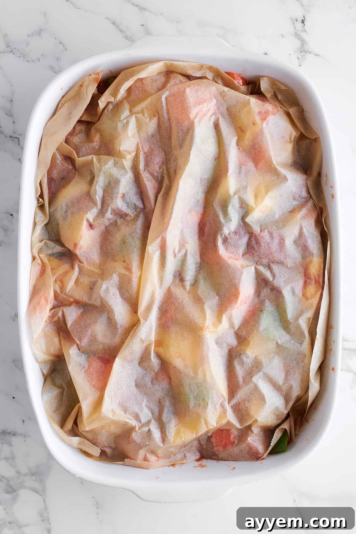 A baking dish, securely covered with both parchment paper and aluminum foil, sits prepared for its time in the oven, sealing in moisture and flavor.