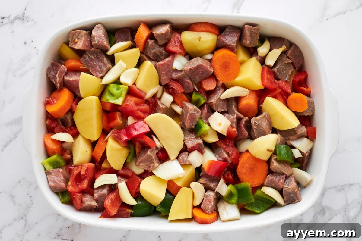 Raw stew meat and sliced veggies in a casserole dish.