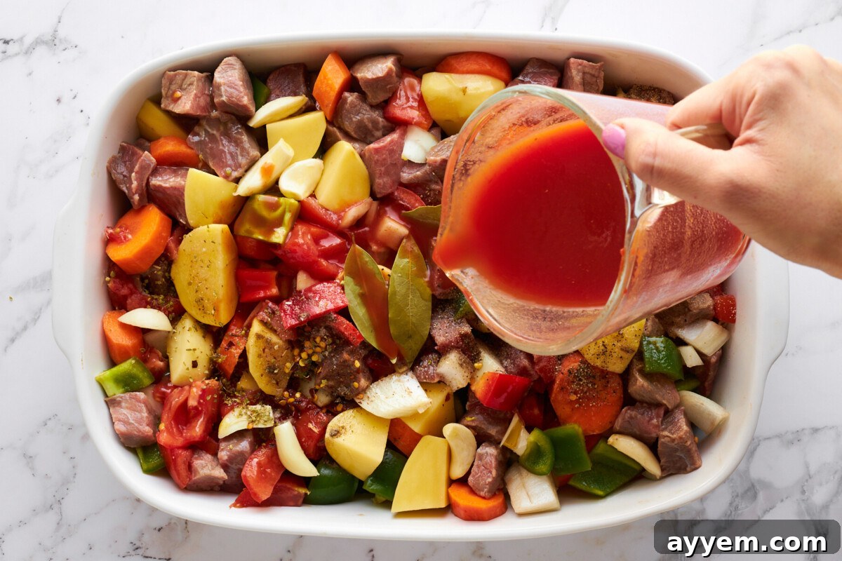 Tomato sauce being poured over beef and veggies in a casserole dish.