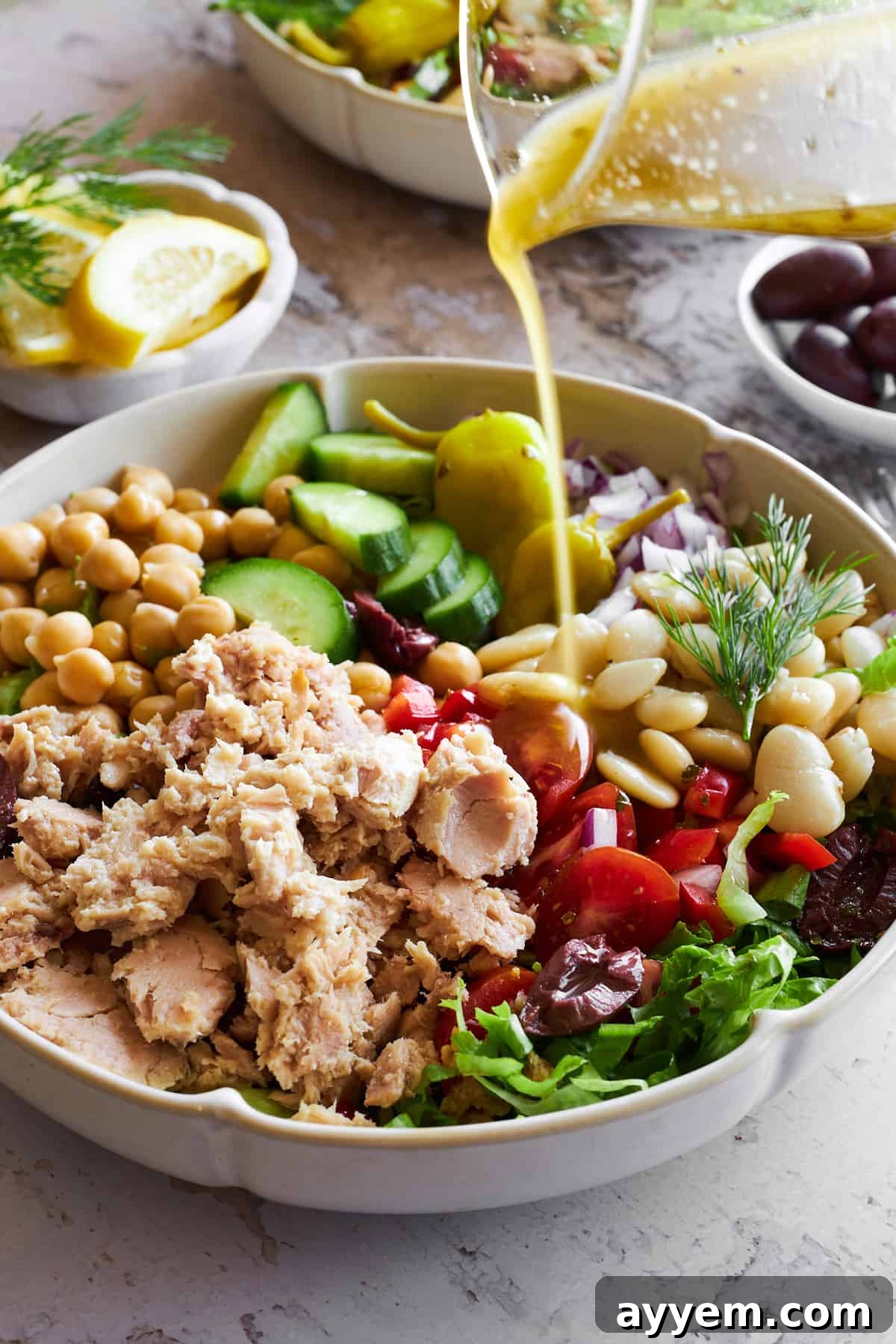 Freshly made vinaigrette being poured over a bountiful bowl of Mediterranean tuna salad, highlighting its vibrant colors.