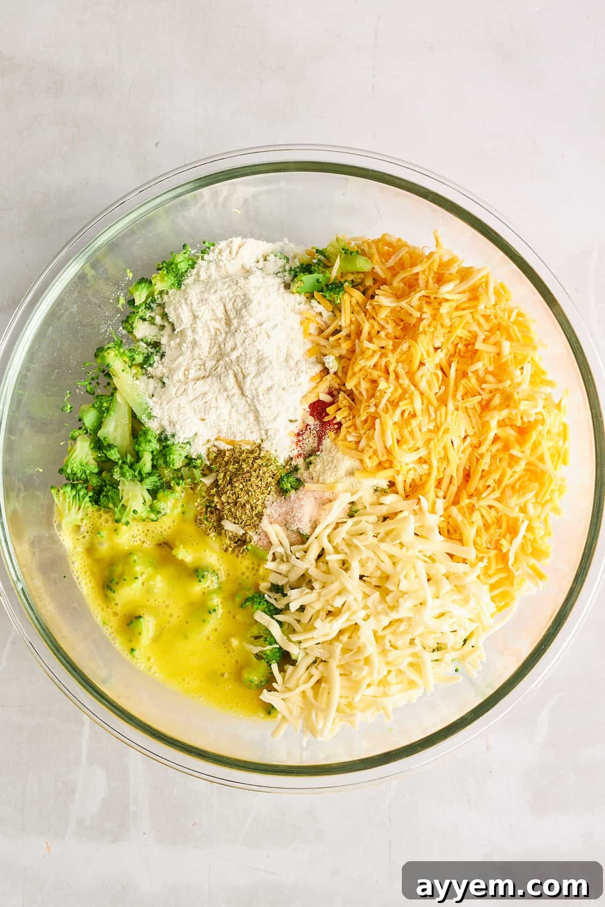 A selection of ingredients for broccoli fritters, including cheese, flour, and spices, in separate bowls.