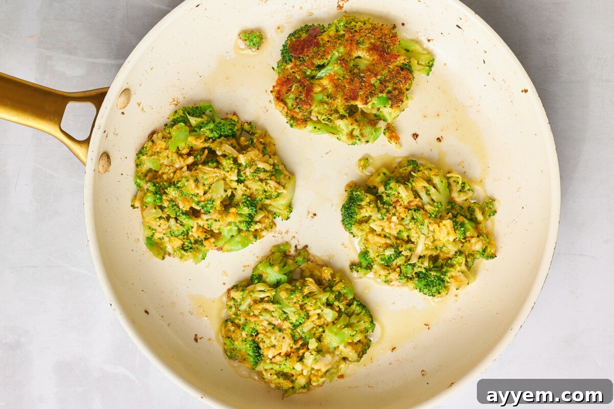 Four cheesy broccoli fritters in a skillet.
