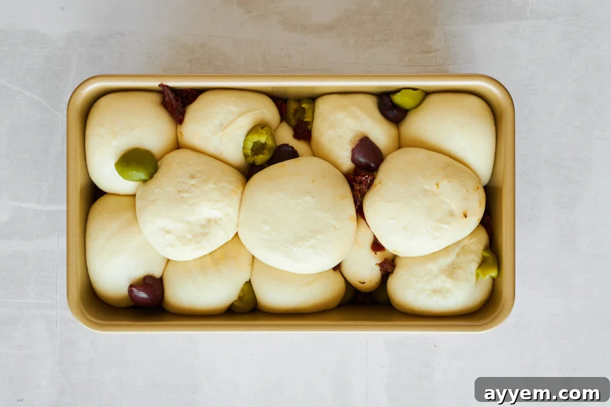 Raw dinner rolls topped with kalamata olives and sun-dried tomatoes.