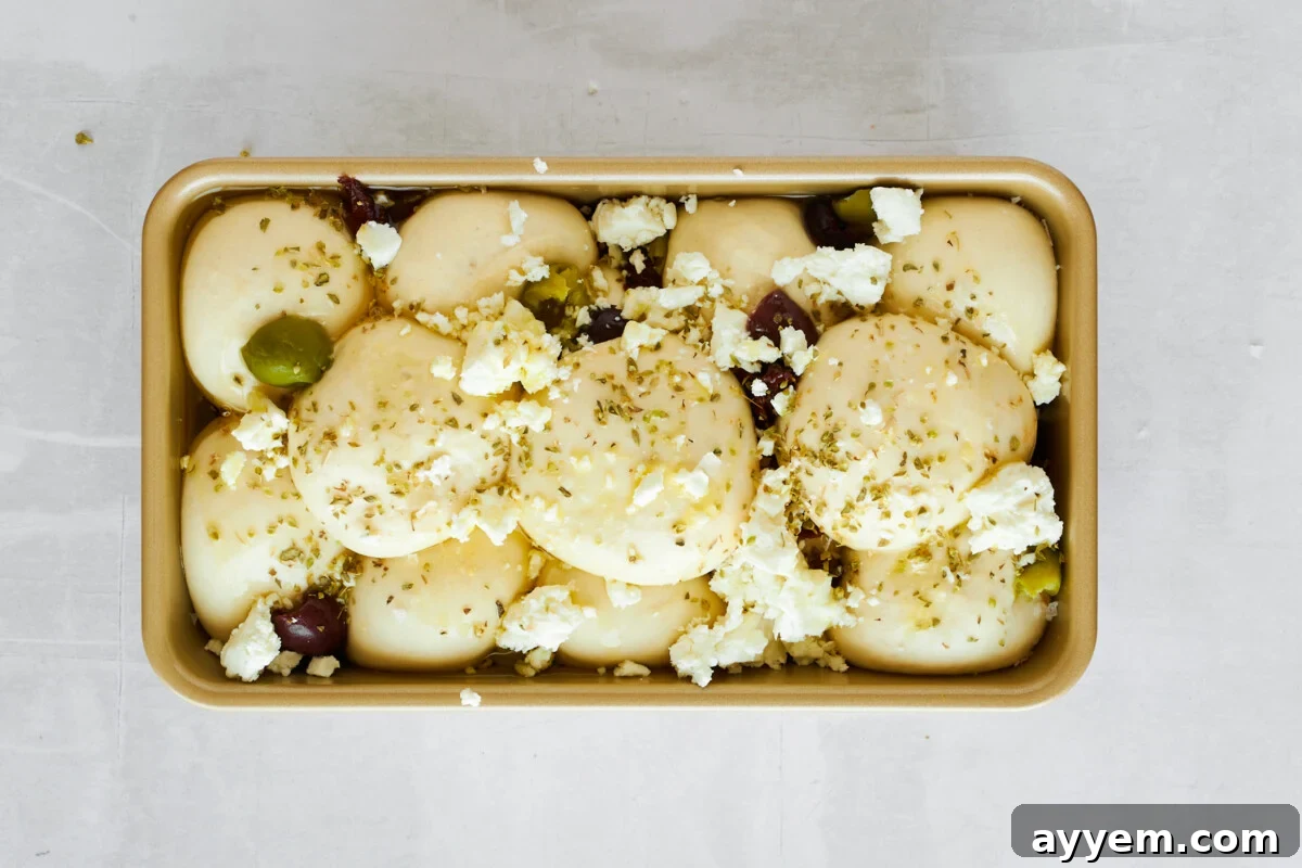 Raw dinner rolls topped with kalamata olives and sun-dried tomatoes and feta.