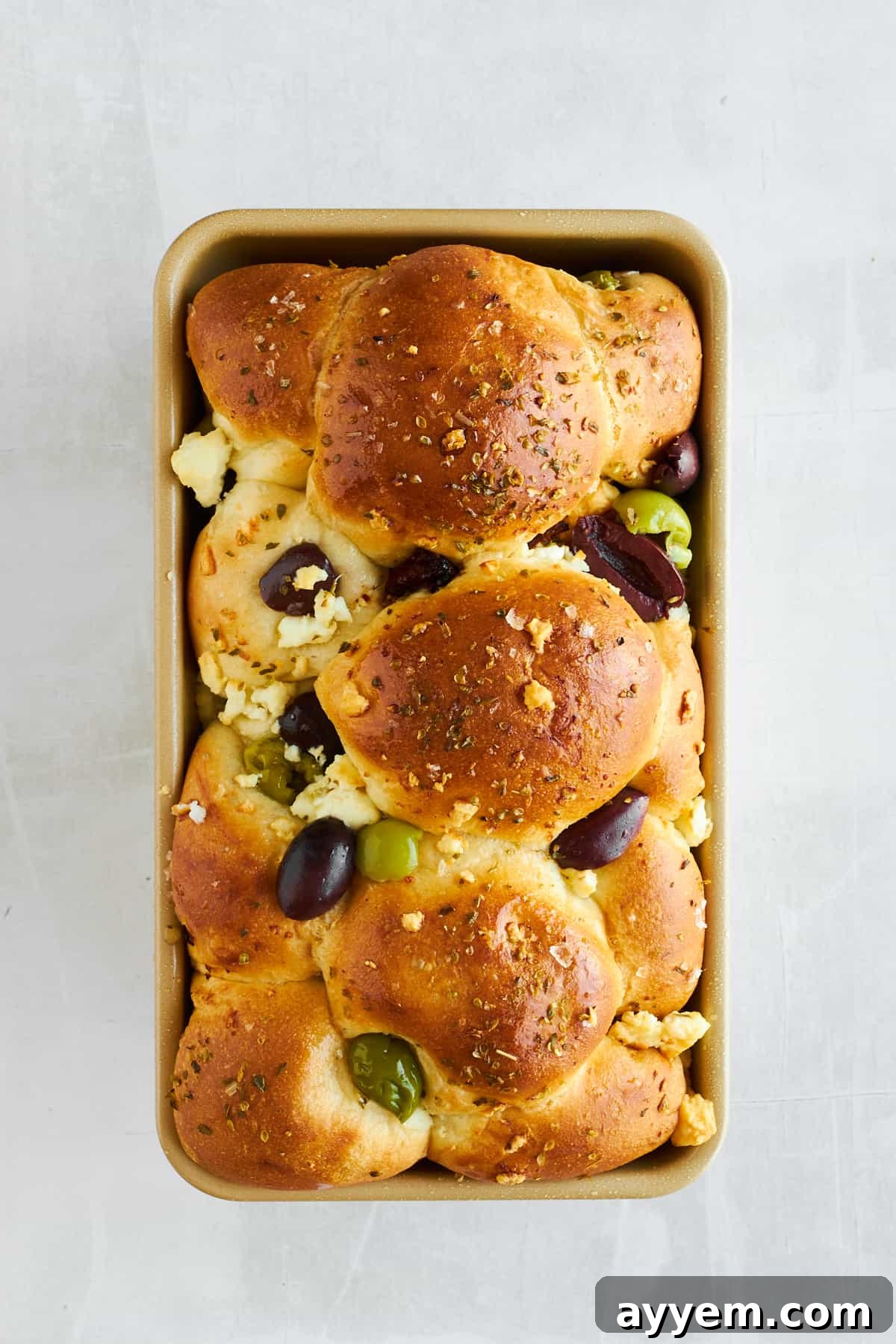 A freshly baked loaf of feta olive bread still warm in its bread pan, ready to be served.