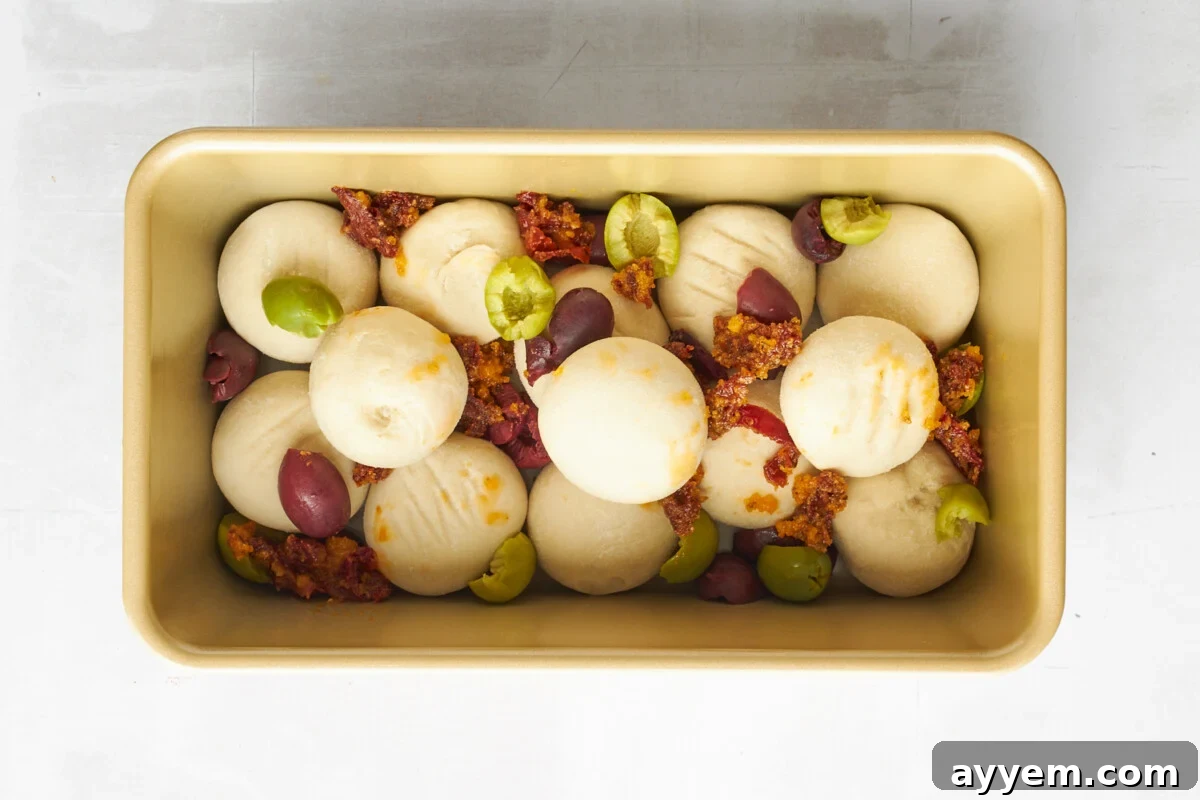 Raw dinner rolls topped with kalamata olives and sun-dried tomatoes.