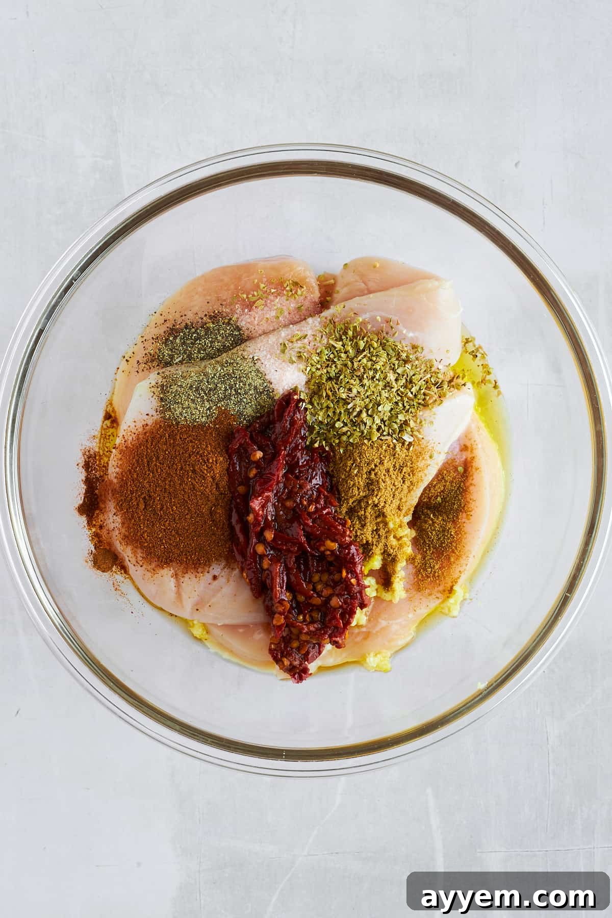 Raw chicken thighs topped with seasonings and oil in a bowl. 
