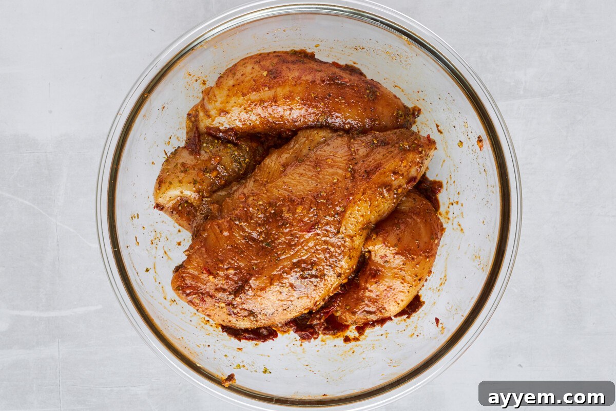 Raw chicken thighs tossed with seasonings in a bowl.