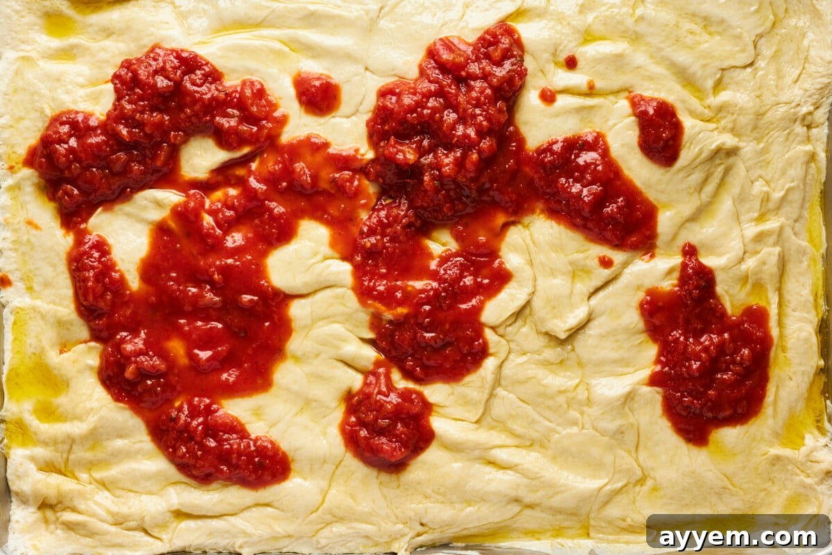 Marinara sauce being spread over the pressed dinner roll crust.