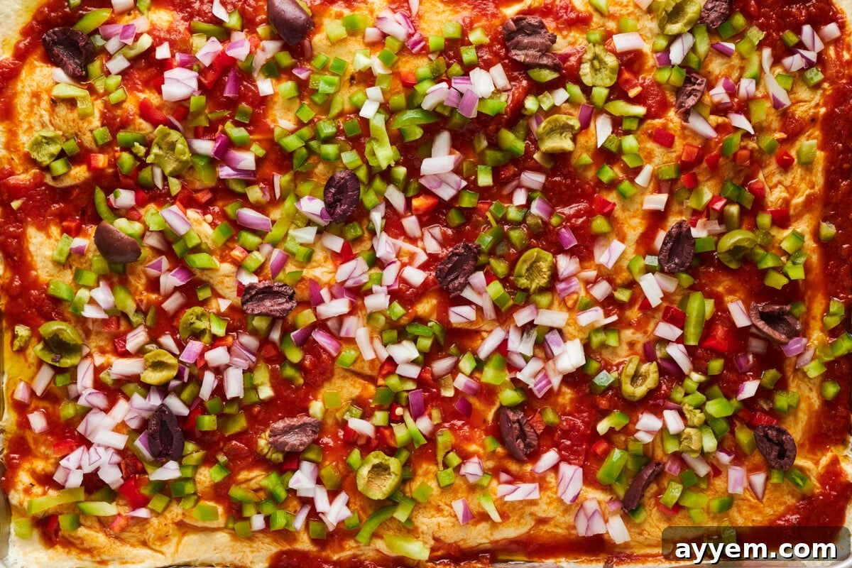 Pizza crust topped with marinara sauce, colorful peppers, onions, and olives.