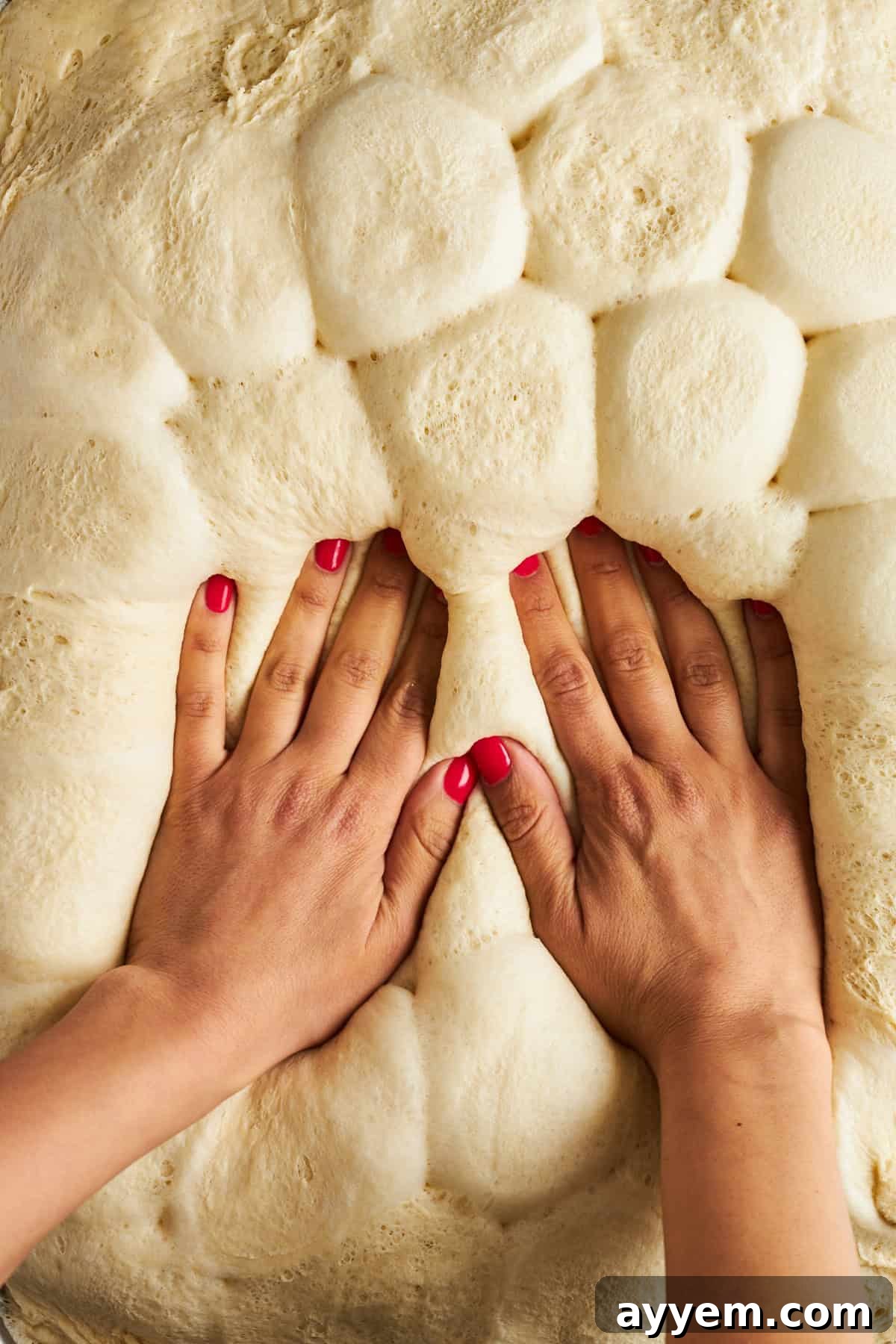 Hands pressing down the risen dinner rolls to form a unified pizza crust.