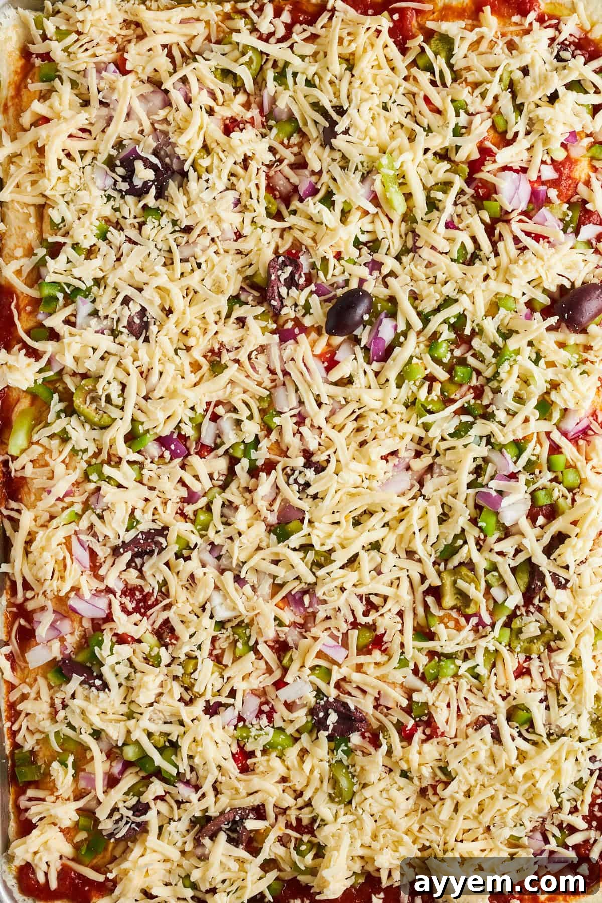 Assembled sheet pan pizza with marinara, veggies, olives, and shredded mozzarella cheese.