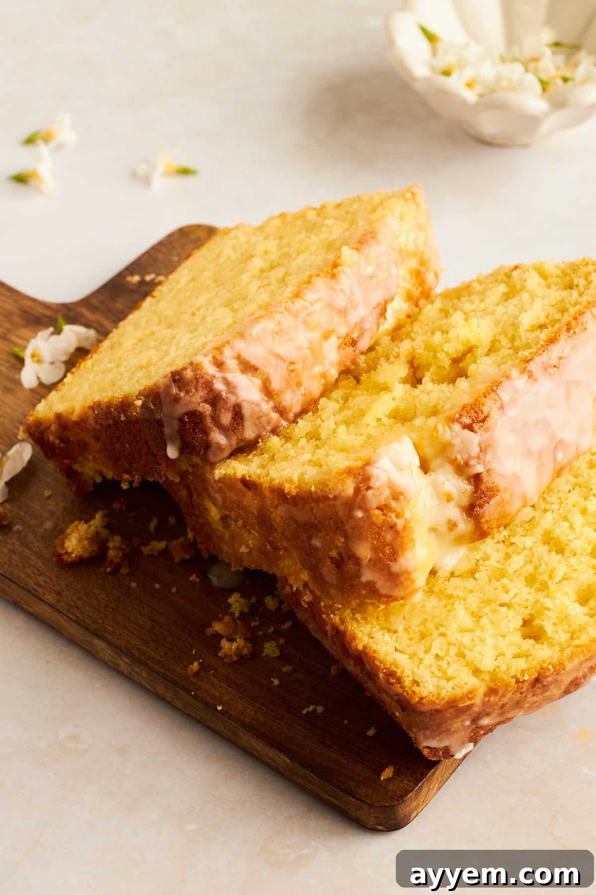 Three slices of perfectly glazed lemon bread displayed on a rustic wooden board, ready to be enjoyed.