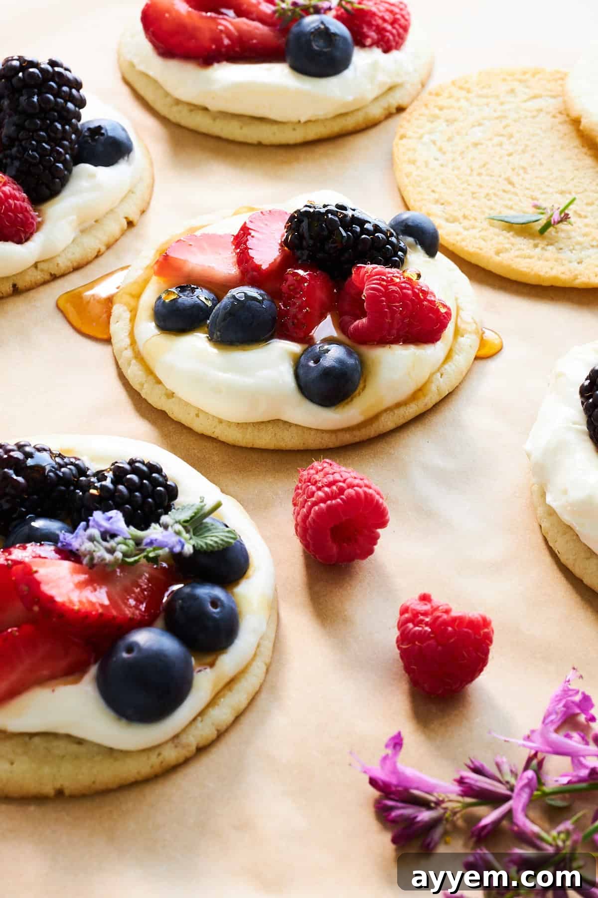 Vibrant Fruit Pizza Cookies with creamy cheesecake icing, an assortment of fresh berries, and a delicate drizzle of honey, ready to be enjoyed.