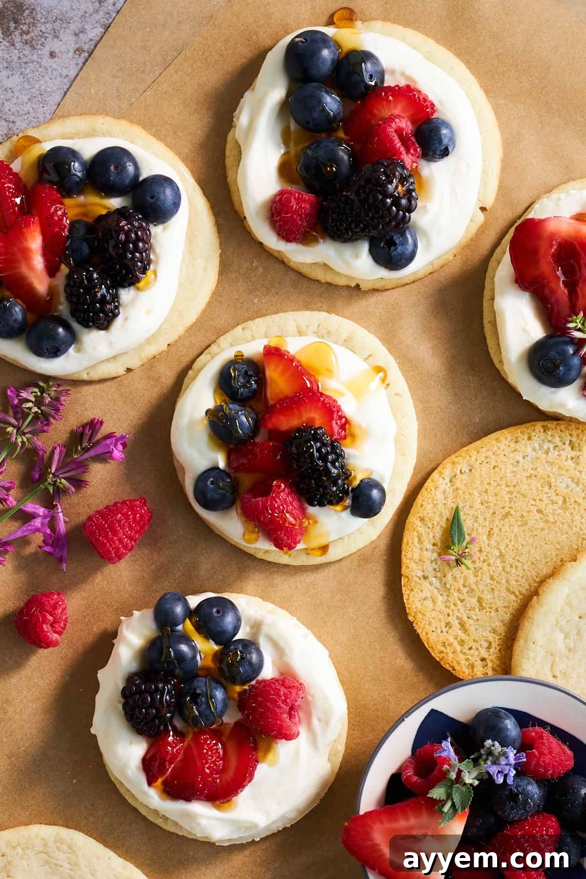 Assembled Fruit Pizza Cookies featuring a cheesecake icing base and an array of fresh berries, garnished with honey.