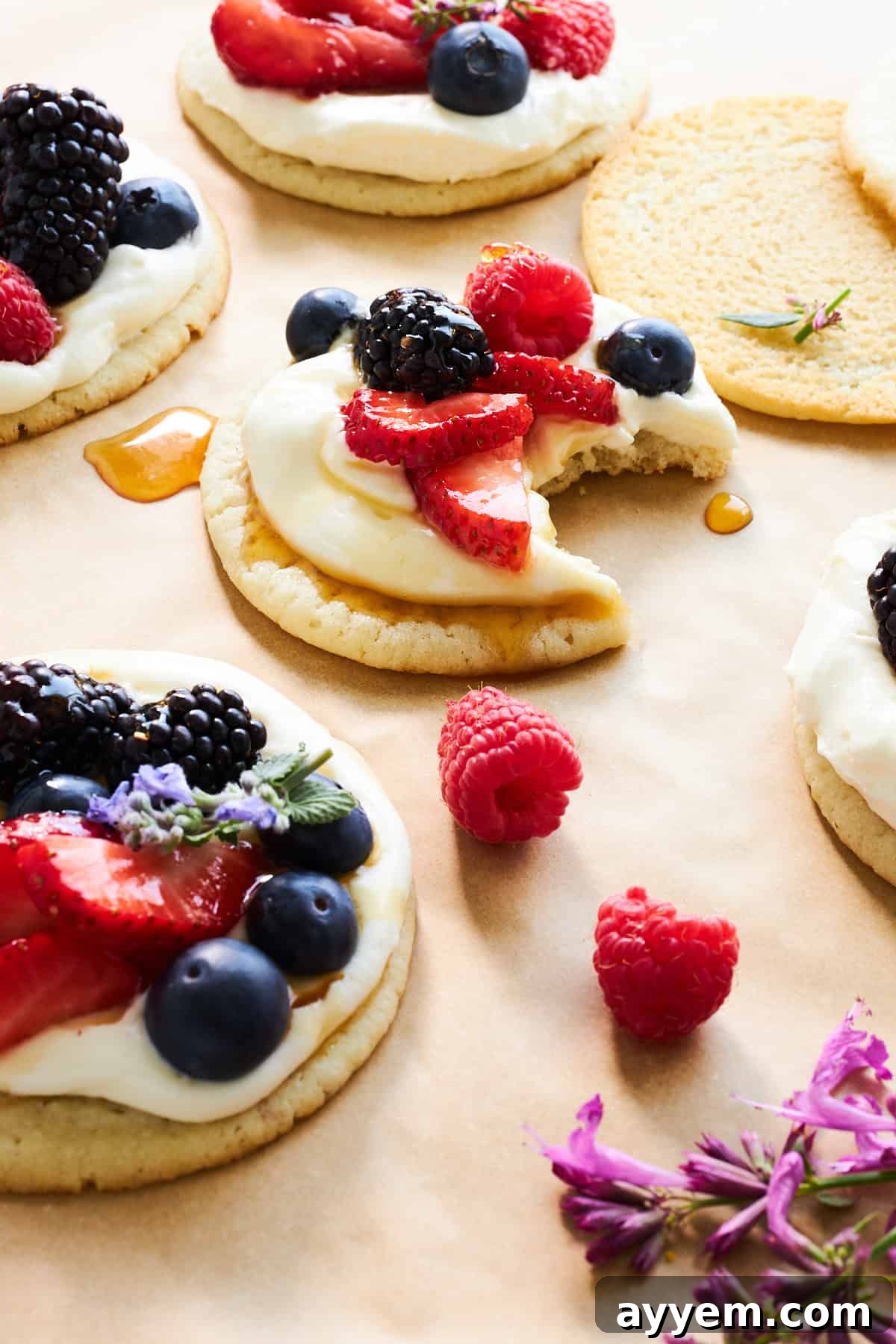 A plate of Fruit Pizza Cookies topped with fresh berries, one with a bite taken out, showcasing the delicious layers.