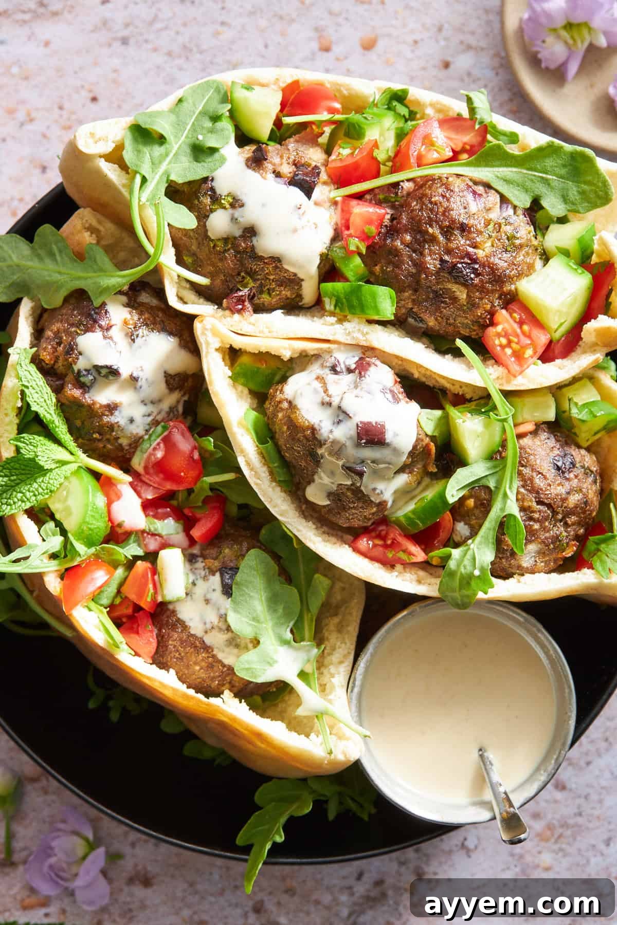 Pita pockets stuffed with vibrant tomato and cucumber salad, perfectly cooked Mediterranean beef meatballs, and creamy tzatziki sauce, showcasing a delicious and healthy meal option.