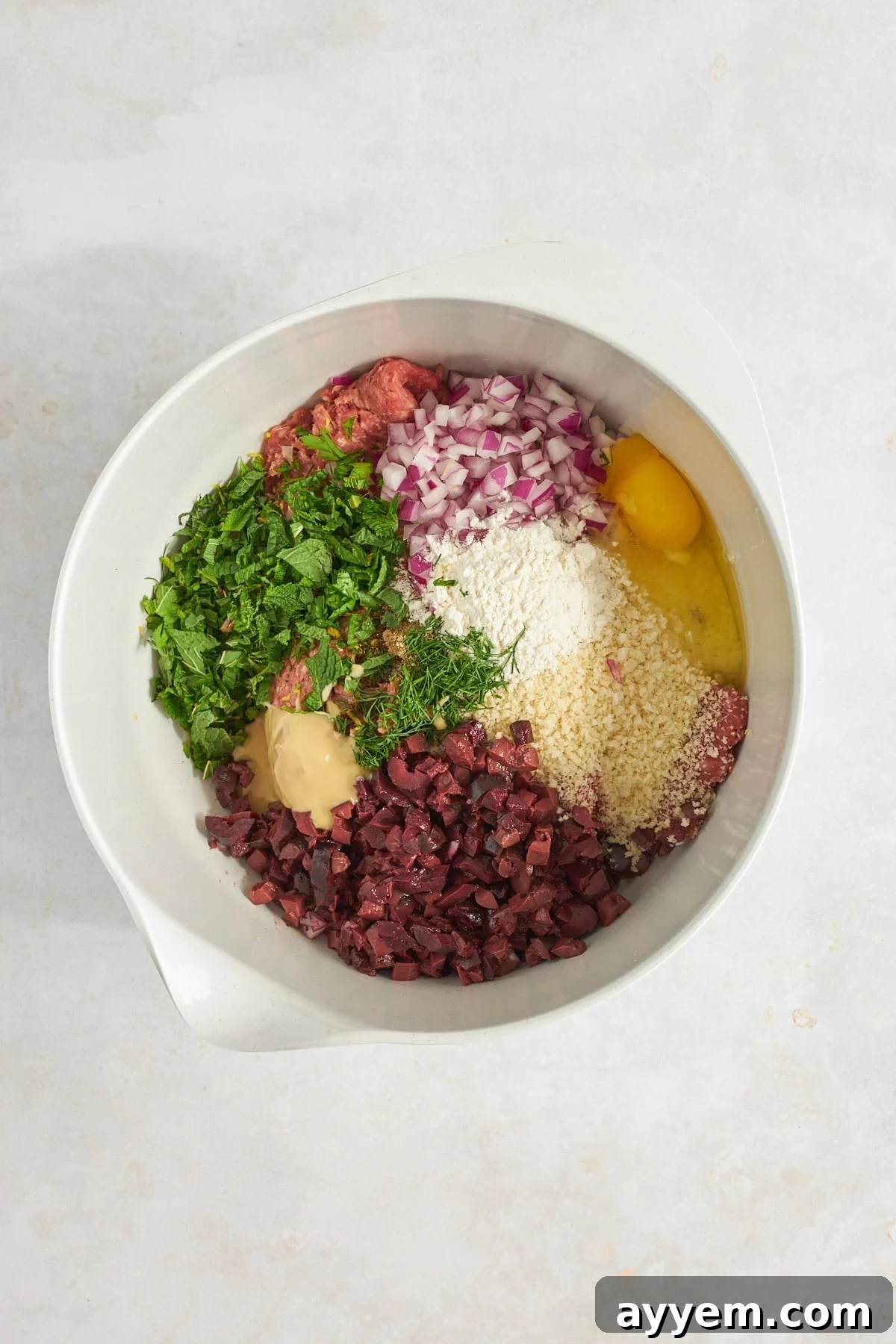 All the fresh ingredients for ground beef meatballs gathered in a mixing bowl, ready to be combined. 