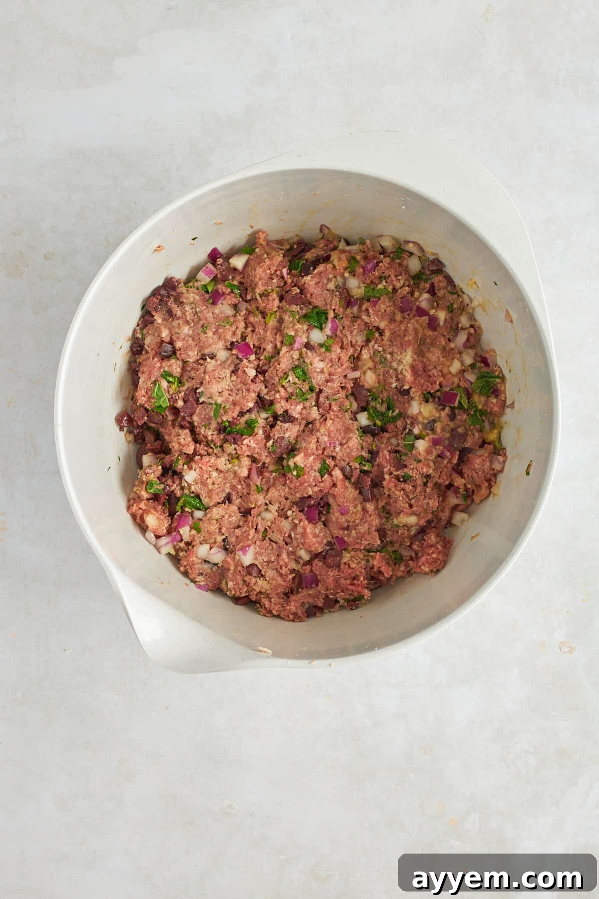 A close-up of the Mediterranean ground beef meatball mixture in a bowl, showing the finely chopped herbs and olives evenly distributed. 