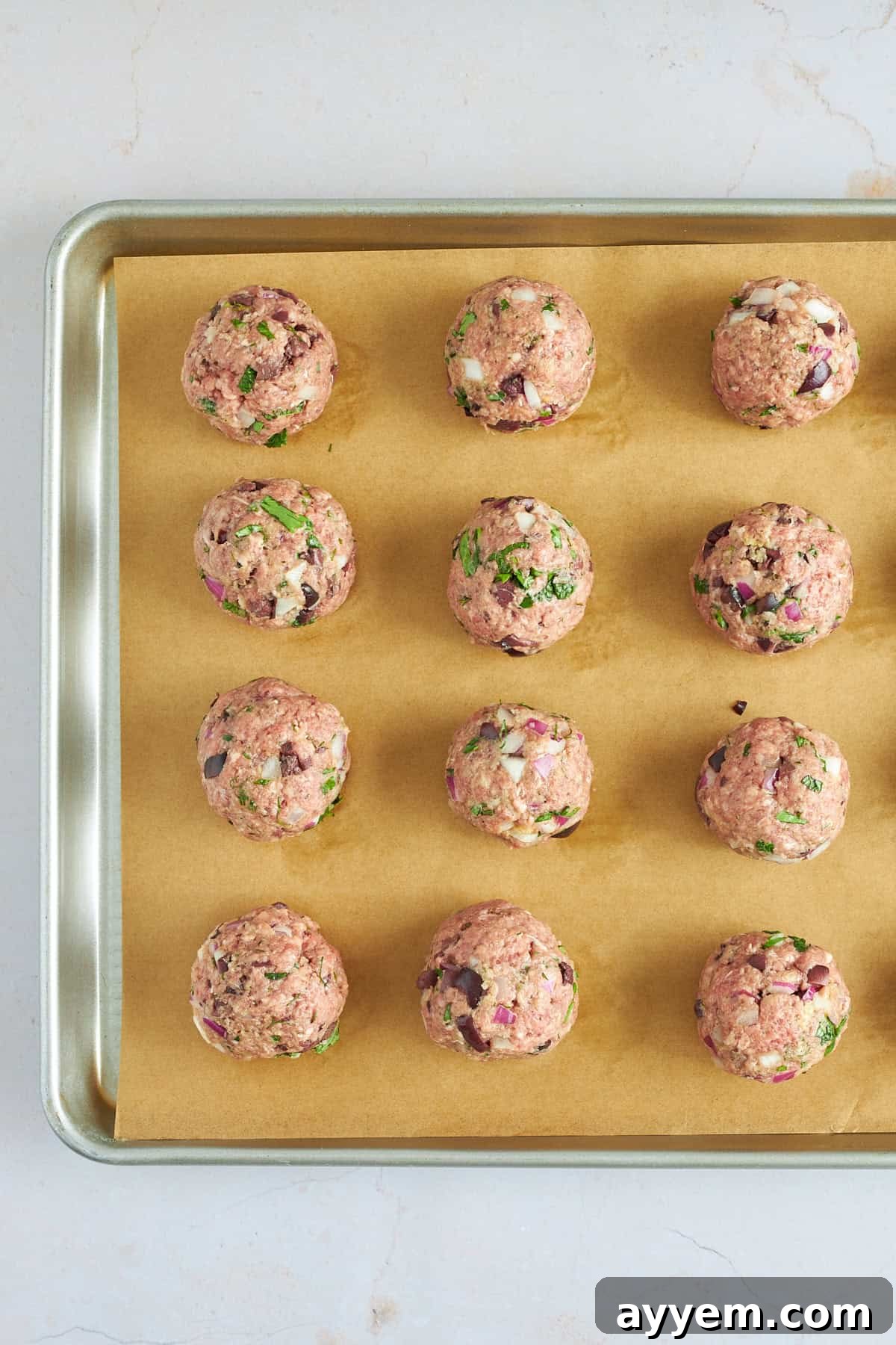Raw, uniformly sized beef meatballs arranged neatly on a baking sheet lined with parchment paper, ready for baking. 