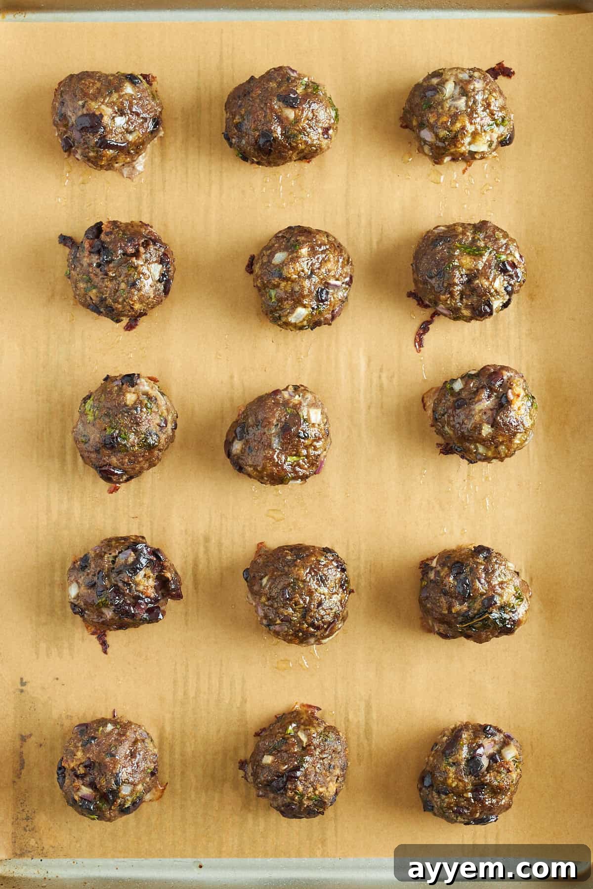 Baked Mediterranean ground beef meatballs, perfectly golden brown and cooked, resting on a parchment paper lined baking sheet. 