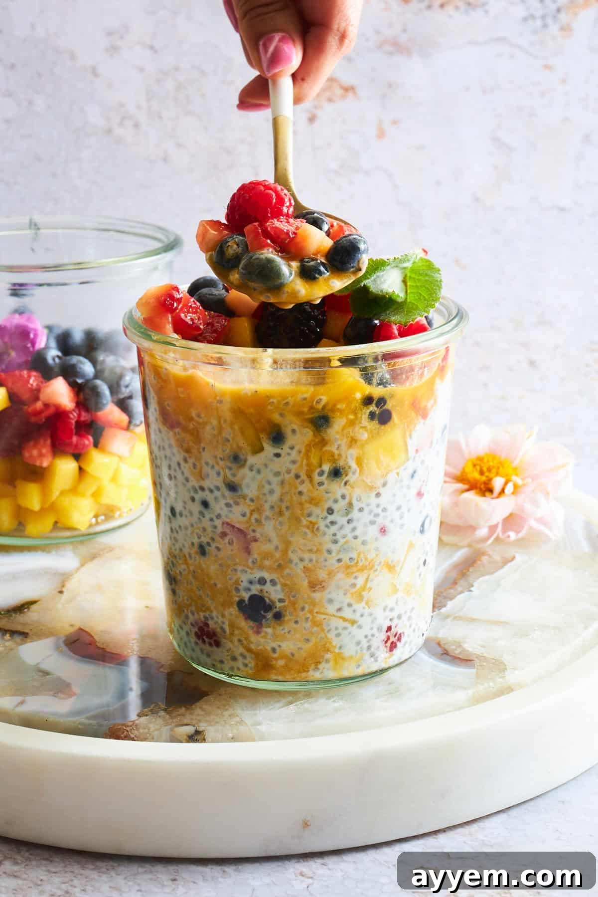 Tropical Mango Chia Pudding with Fresh Fruit Medley 4 A beautifully presented jar of mango chia pudding with fruit salad, featuring a spoon scooping out a portion, highlighting its inviting texture.