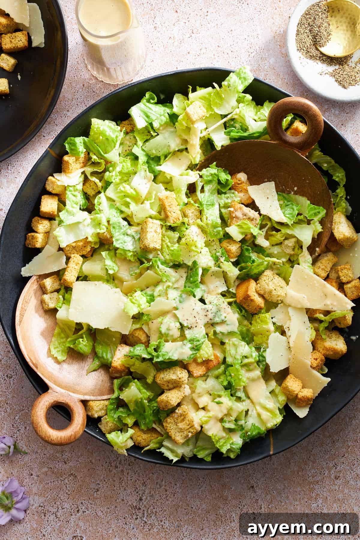 Overhead image of a bowl of Caesar salad topped with a rich dressing, ready to be served.