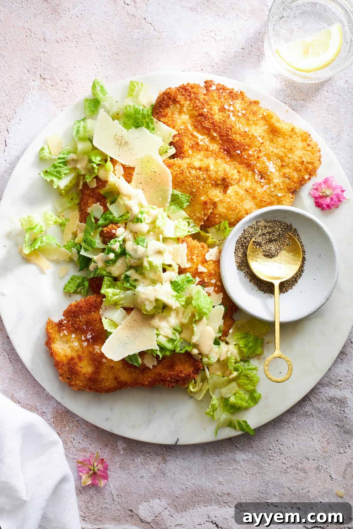 Golden Chicken Milanese with Zesty Caesar Salad 2 A plate of golden-brown chicken Milanese topped with a generous serving of crisp Caesar salad.