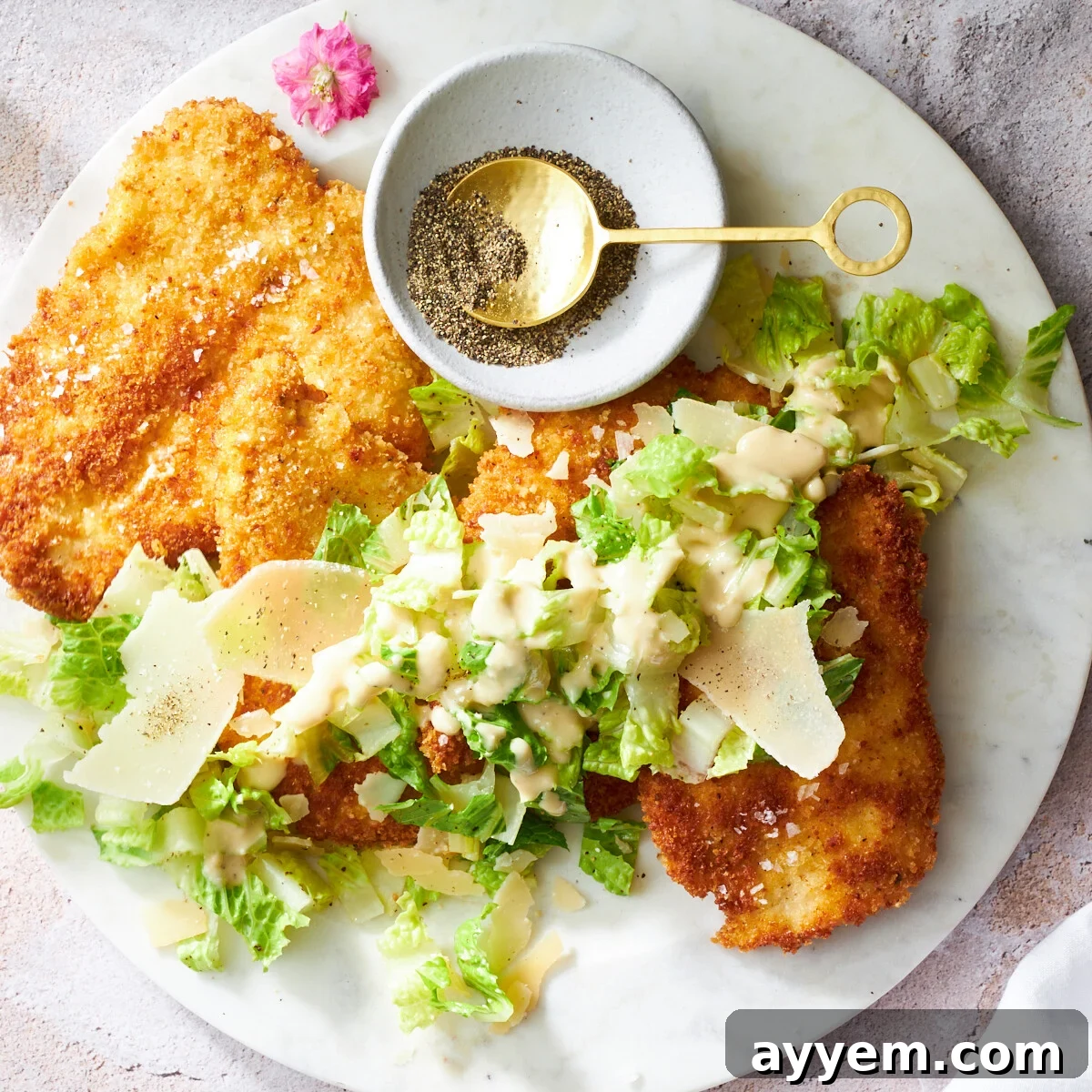 A plate of golden-brown chicken Milanese topped with a generous serving of crisp Caesar salad.