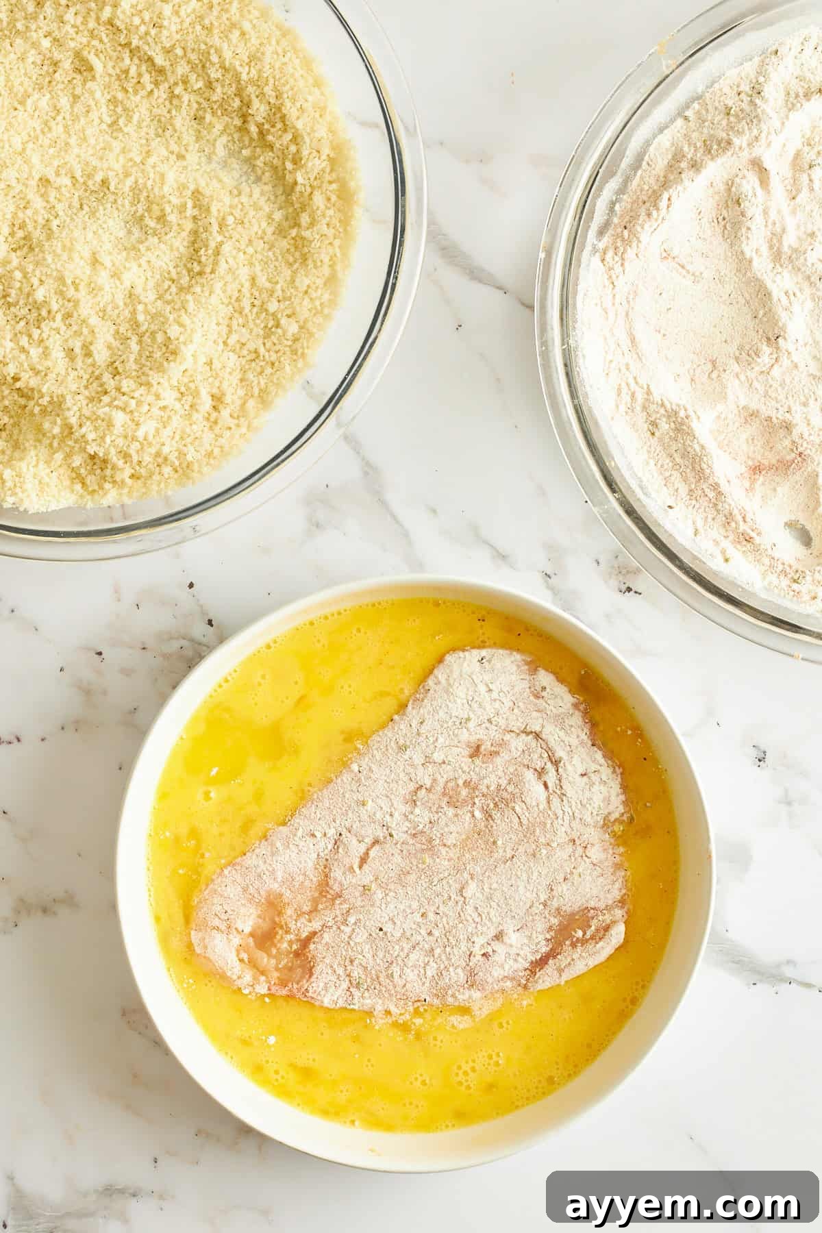 Golden Chicken Milanese with Zesty Caesar Salad 7 A floured chicken cutlet being dipped into a bowl of whisked eggs, ensuring a complete and even liquid coating.