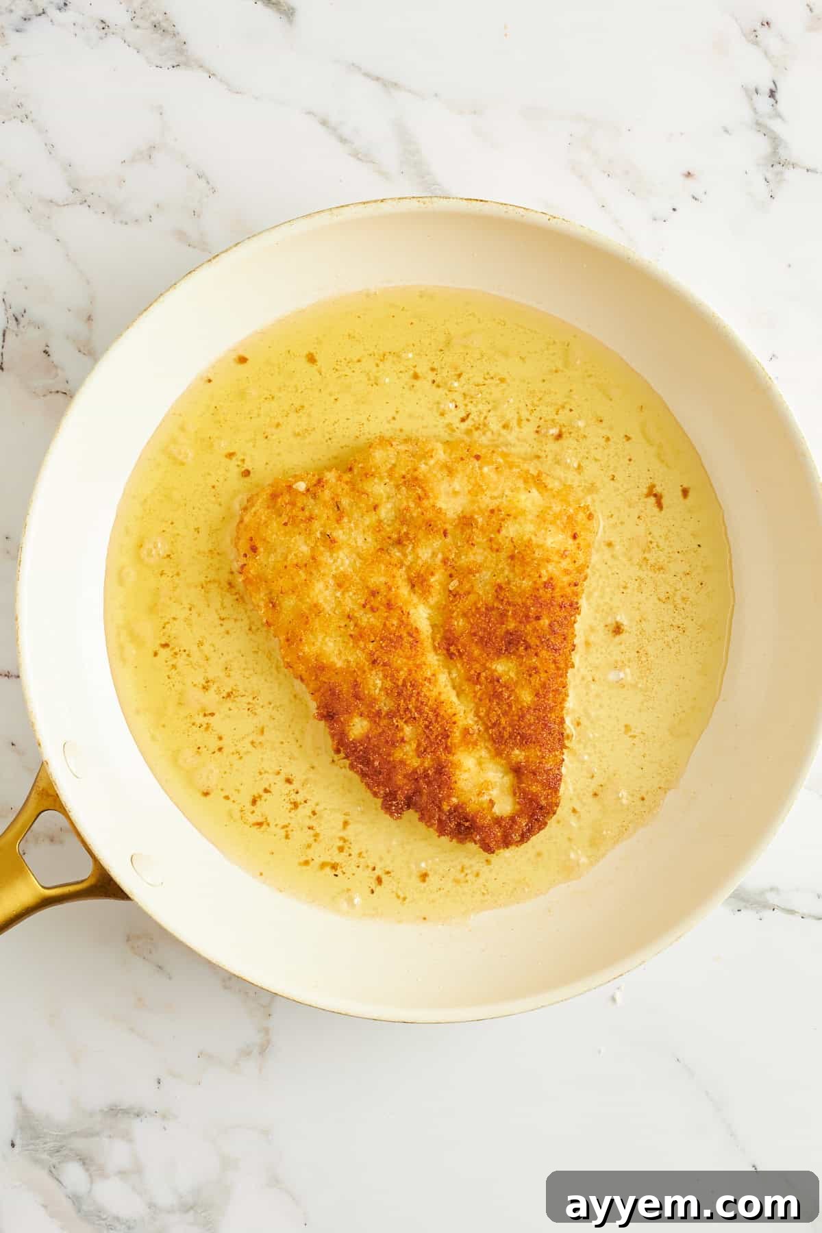Golden Chicken Milanese with Zesty Caesar Salad 9 A breaded chicken breast sizzling and turning golden in a hot skillet with cooking spray or oil, showcasing the pan-frying process.