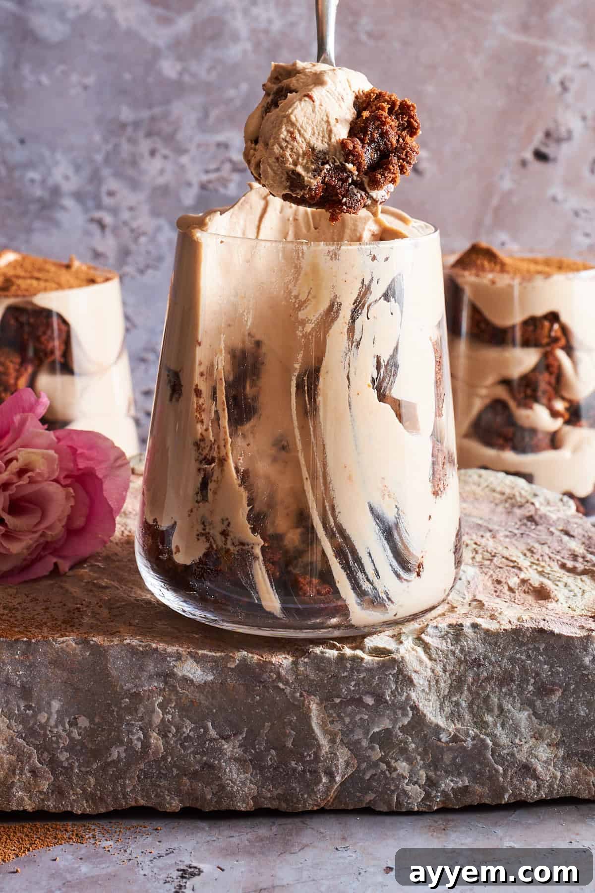 A spoon lifting a bite of tiramisu brownie parfait from a cup, revealing the rich layers.