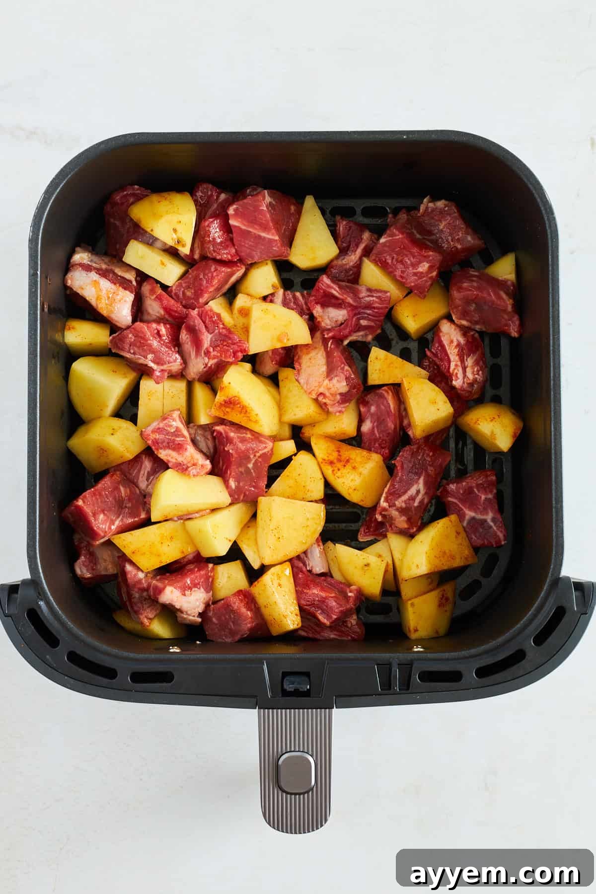 Raw steak and potatoes, seasoned with spices and olive oil, arranged on a tray, ready for air frying.