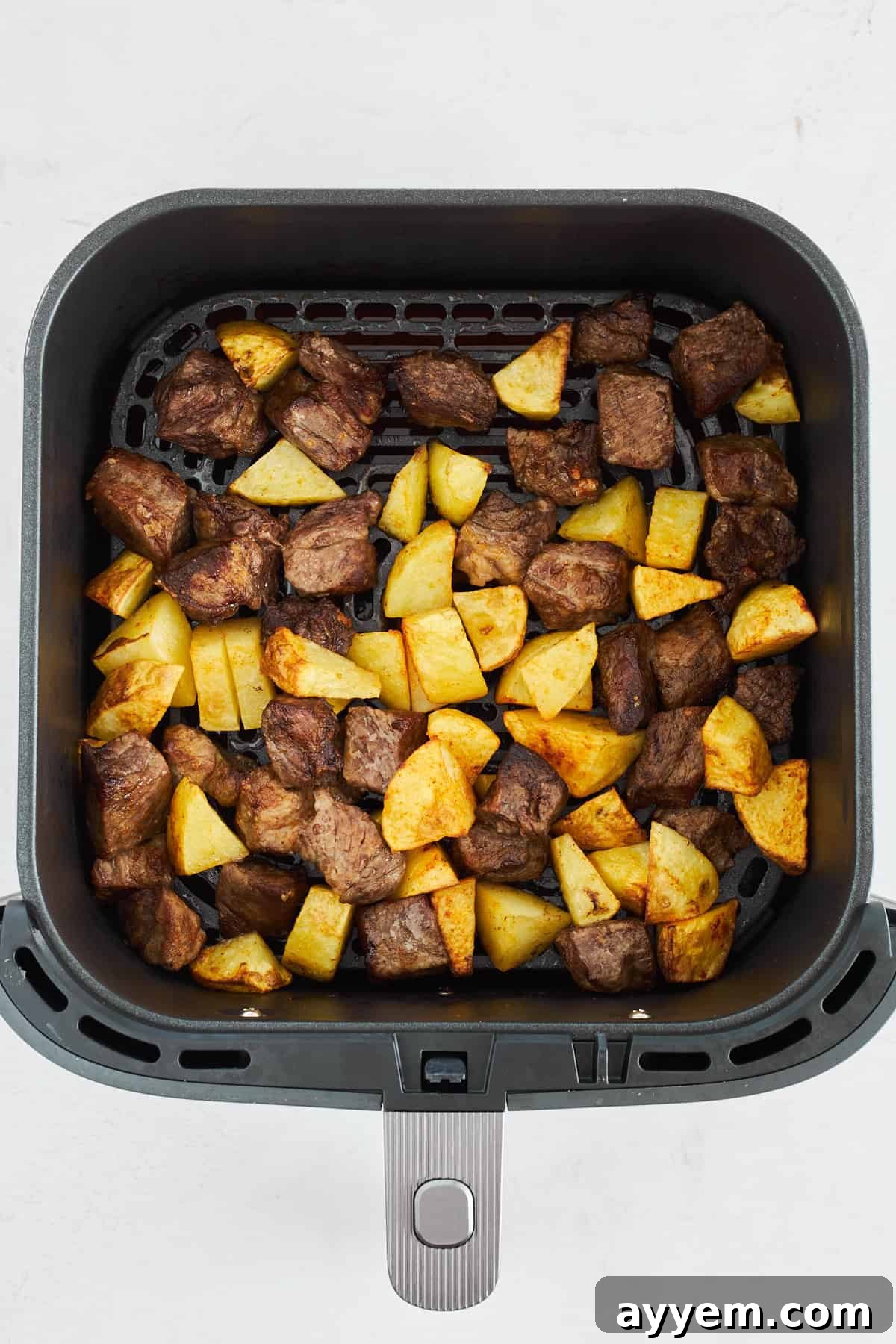 Cooked steak and potato pieces in an air fryer basket, showing crispy golden potatoes and seared steak.