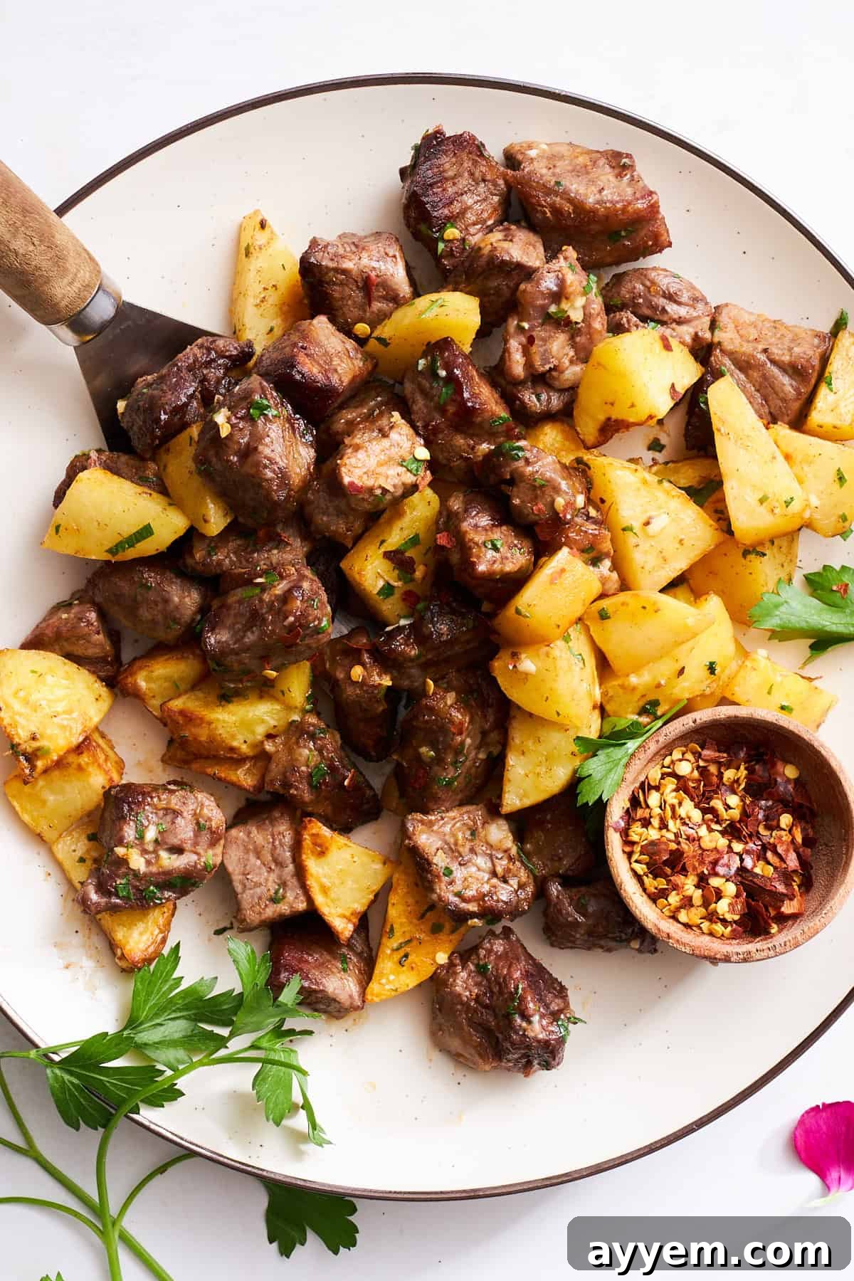 A plate of steak bites and potatoes, garnished with fresh parsley.