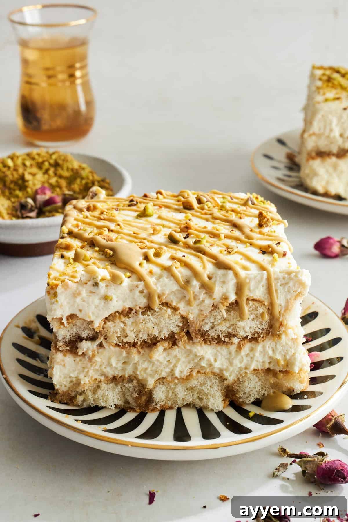 A perfectly portioned slice of vibrant green pistachio tiramisu resting on a white plate, showcasing its distinct layers of creamy mascarpone and coffee-soaked ladyfingers, topped with a generous sprinkle of crushed pistachios.