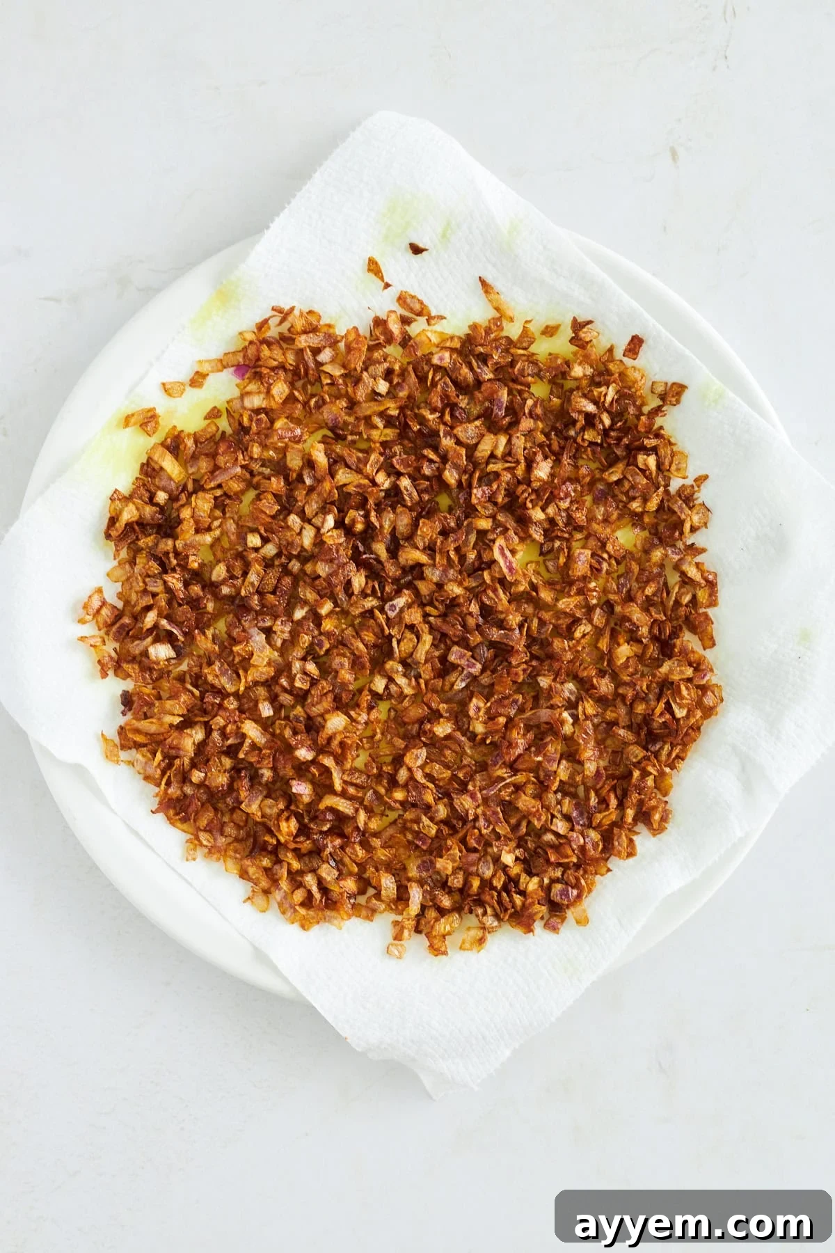 Crispy fried onions draining on a paper towel-lined plate, glistening and golden brown.