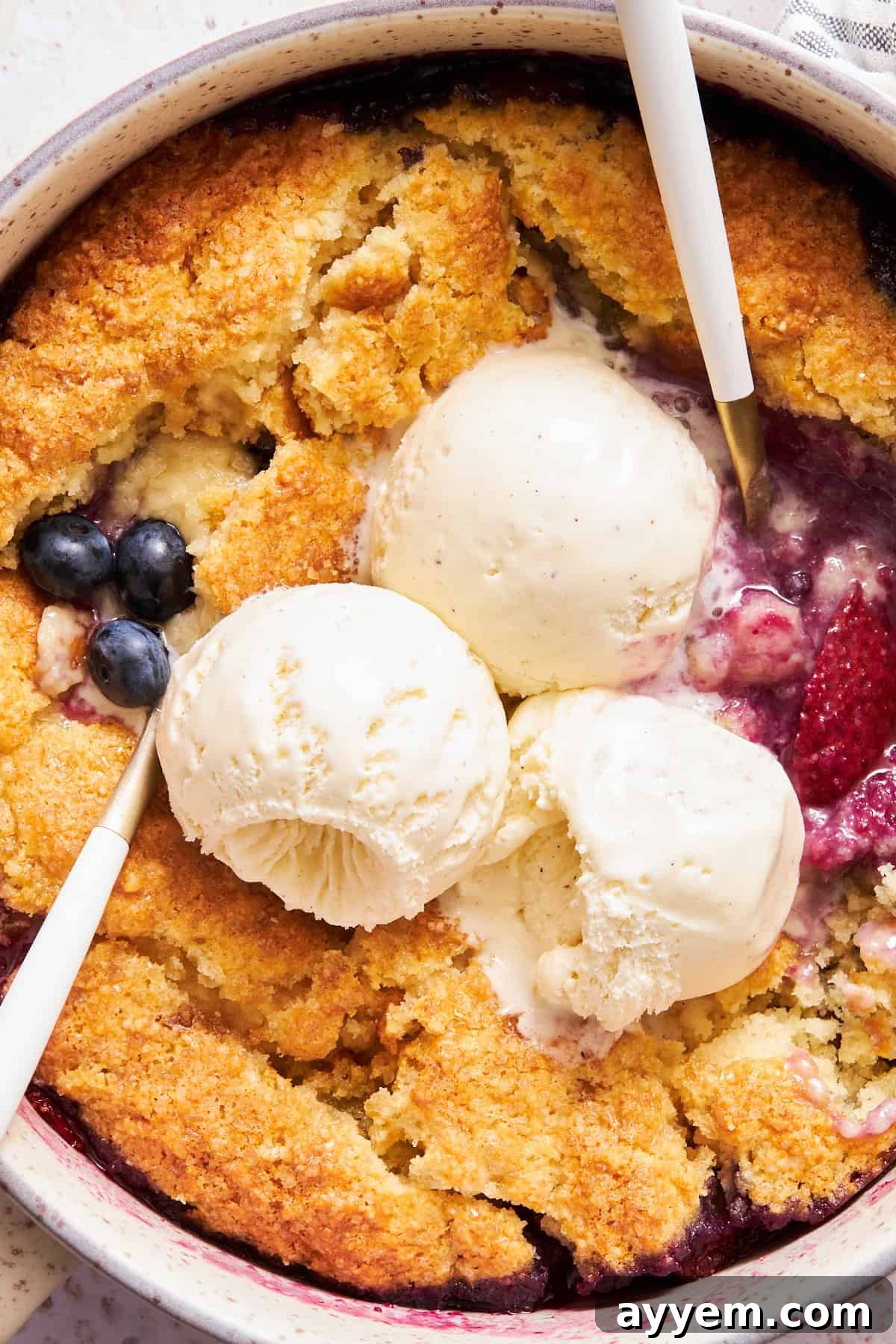 Close up view of mixed berry cobbler topped with three scoops of vanilla ice cream.