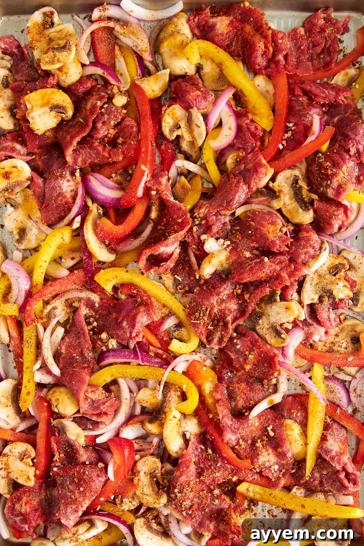 Uncooked Philly cheesesteak ingredients on a baking sheet. 