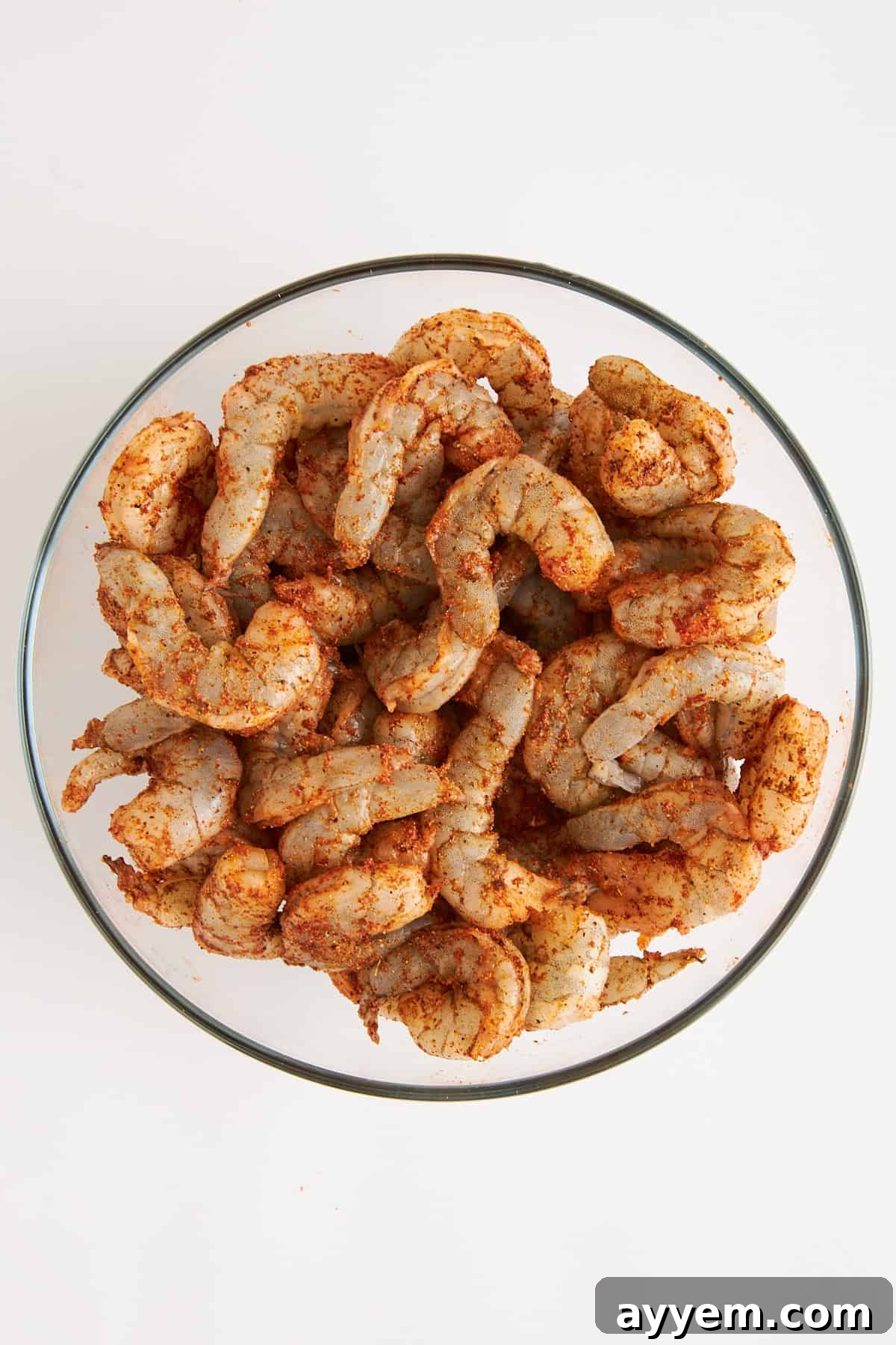 Raw shrimp seasoned with spices in a bowl, ready for cooking.