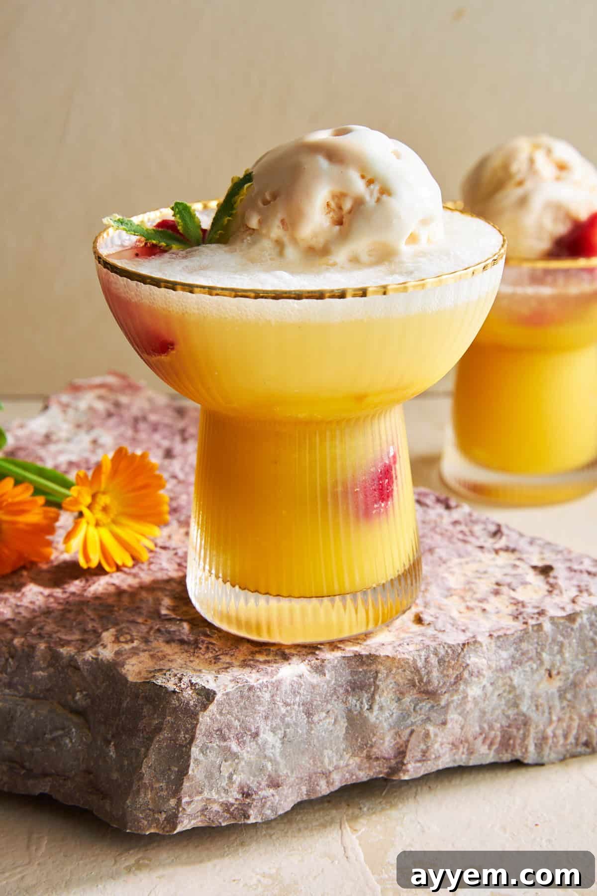 Two glasses of vibrant orange sherbet punch, garnished with fresh strawberries and a scoop of vanilla ice cream, ready for a refreshing treat.