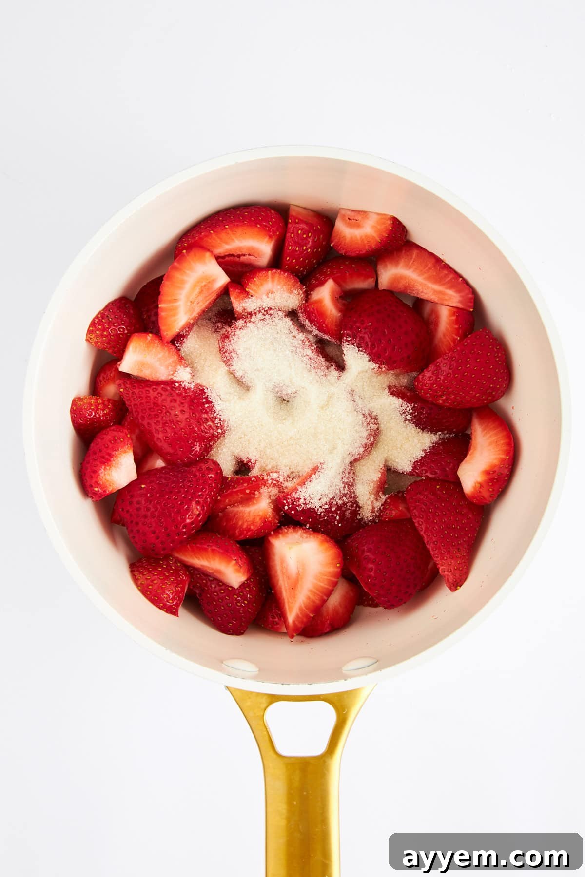Fresh strawberries being combined with granulated sugar in a saucepan, ready for cooking.