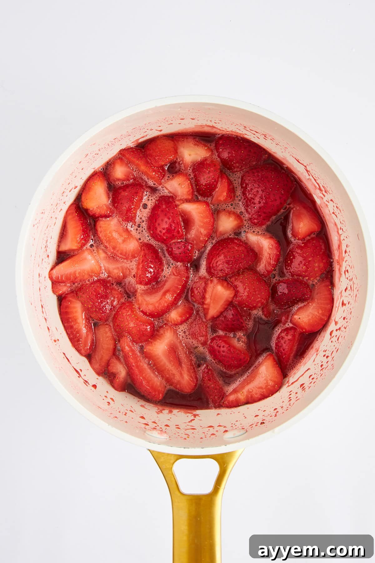 Sliced strawberries gently cooking with sugar in a saucepan, releasing their juices and softening.