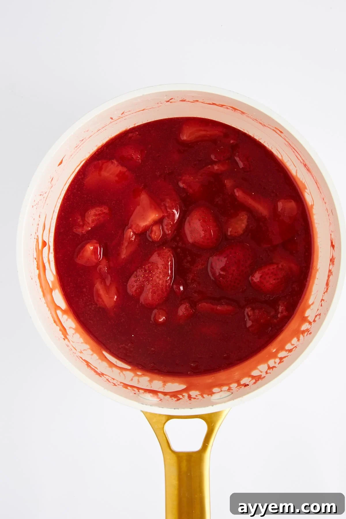 Strawberry sauce simmering in a saucepan, visibly thickening as it cooks.