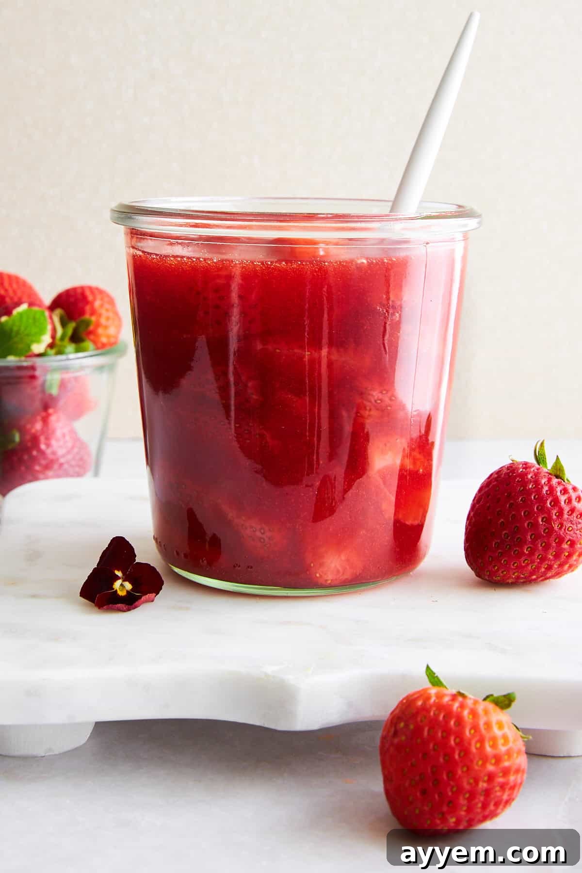 A glass jar filled with luscious homemade strawberry sauce, ready to be served, with a spoon gently resting in it.
